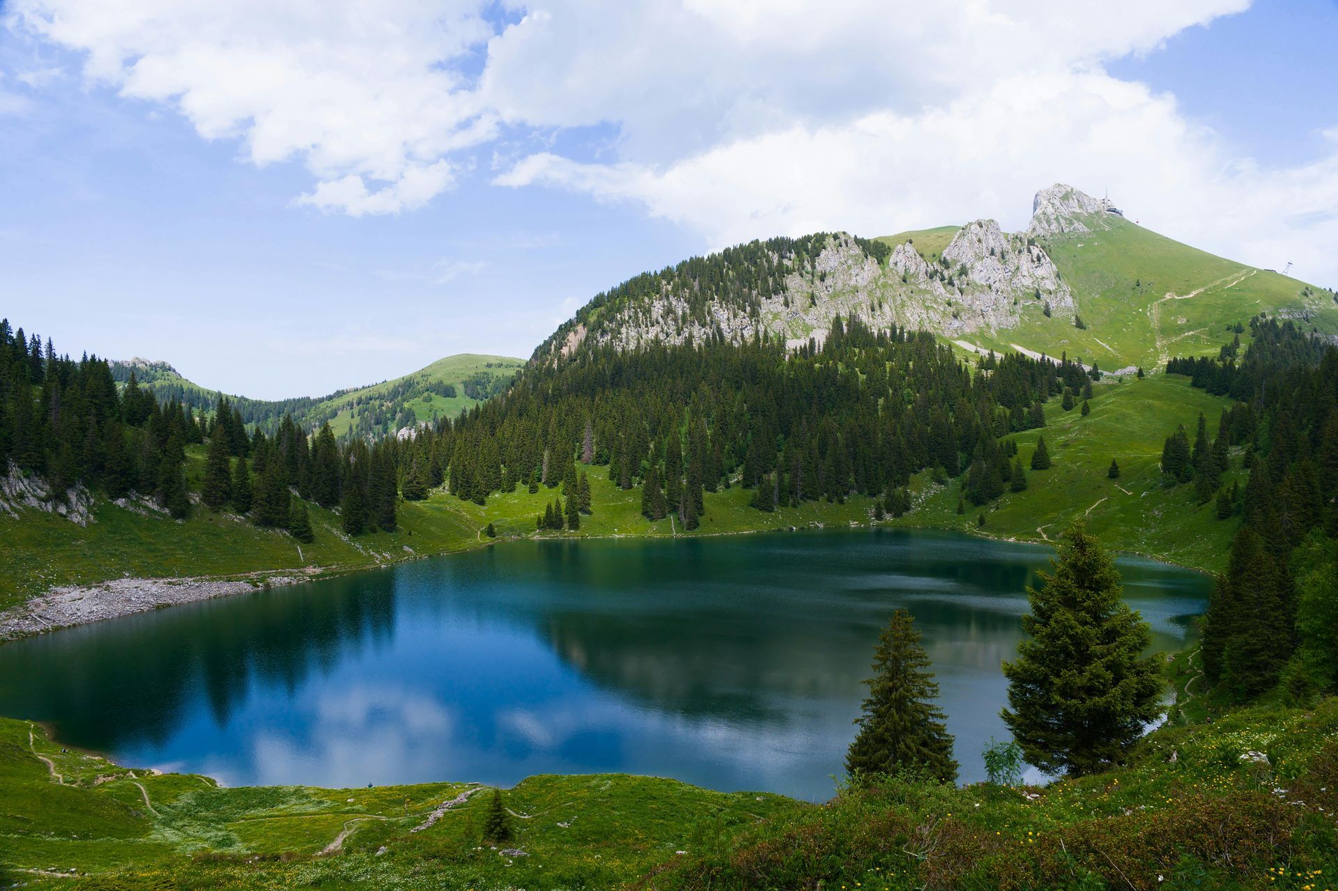 Blue mountain lake surrounded by green forest and rocky hills under a partly cloudy sky