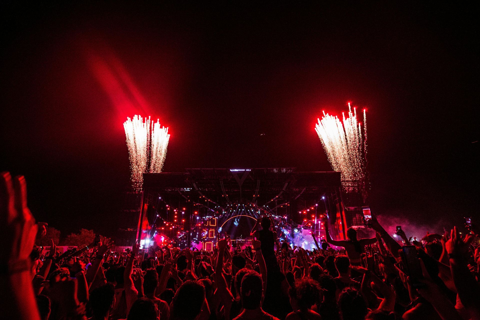 Concert with fireworks. Crowd cheering at a stage lit with red lights.
