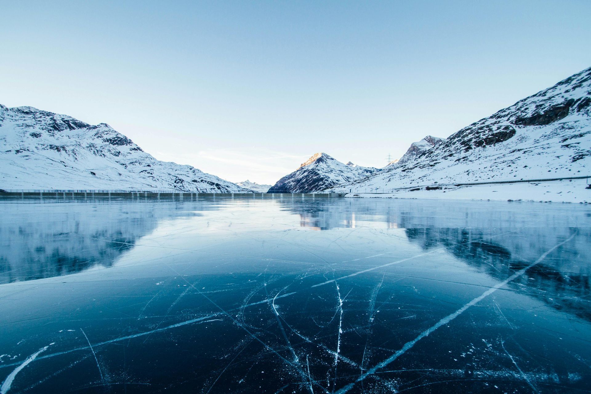 Frozen lake with mountain backdrop under a clear blue sky. Snow covers the mountains.