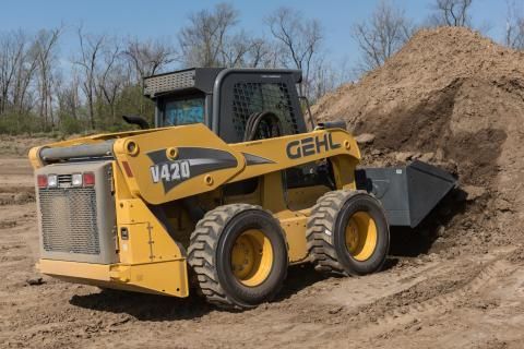 A yellow Gehl V420 skid steer loader works on a dirt pile in an outdoor field.