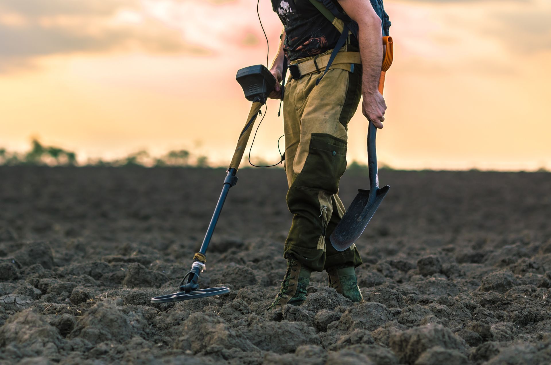 A man is using a metal detector and a shovel in a field