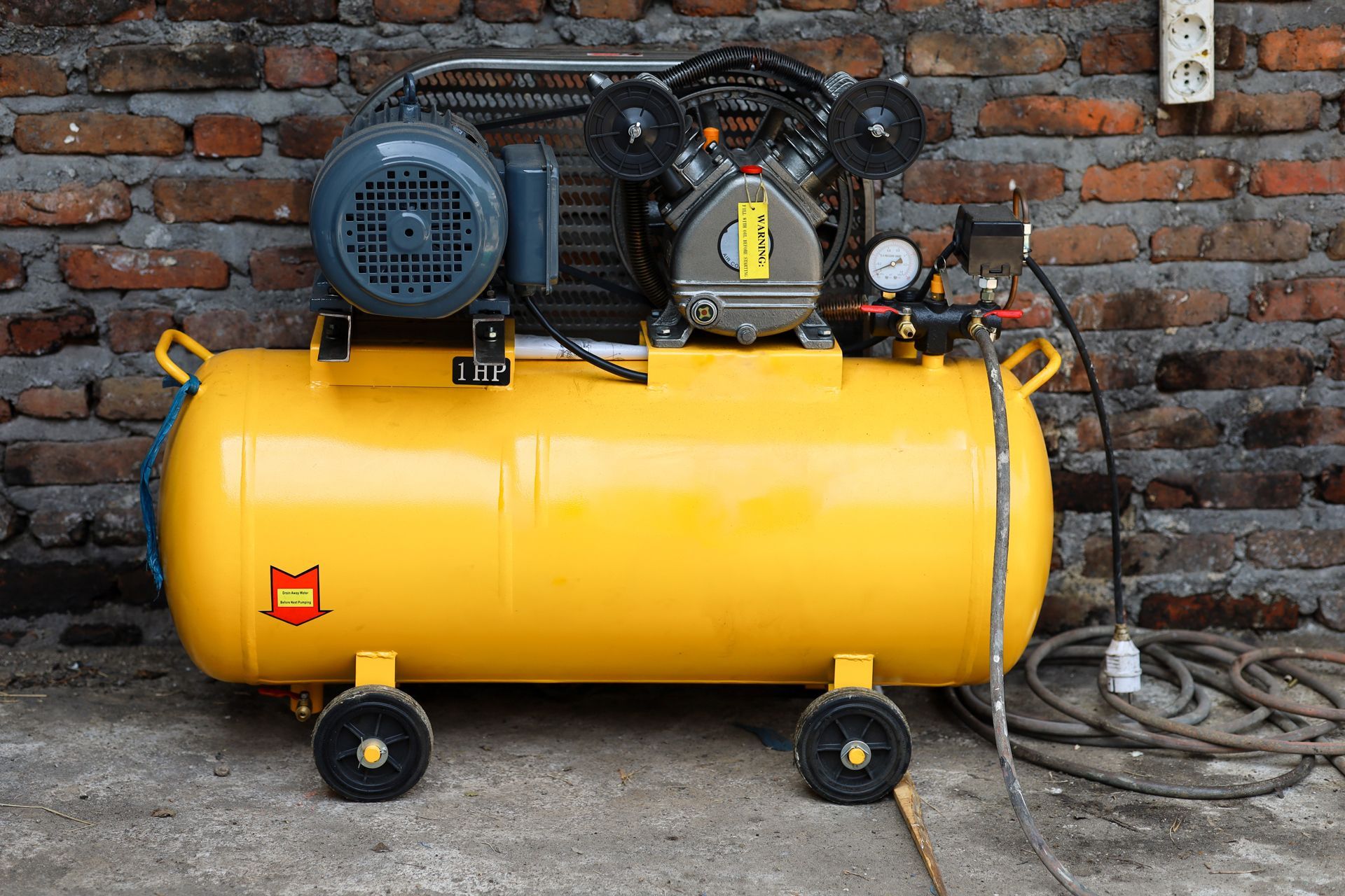 A yellow air compressor is sitting in front of a brick wall