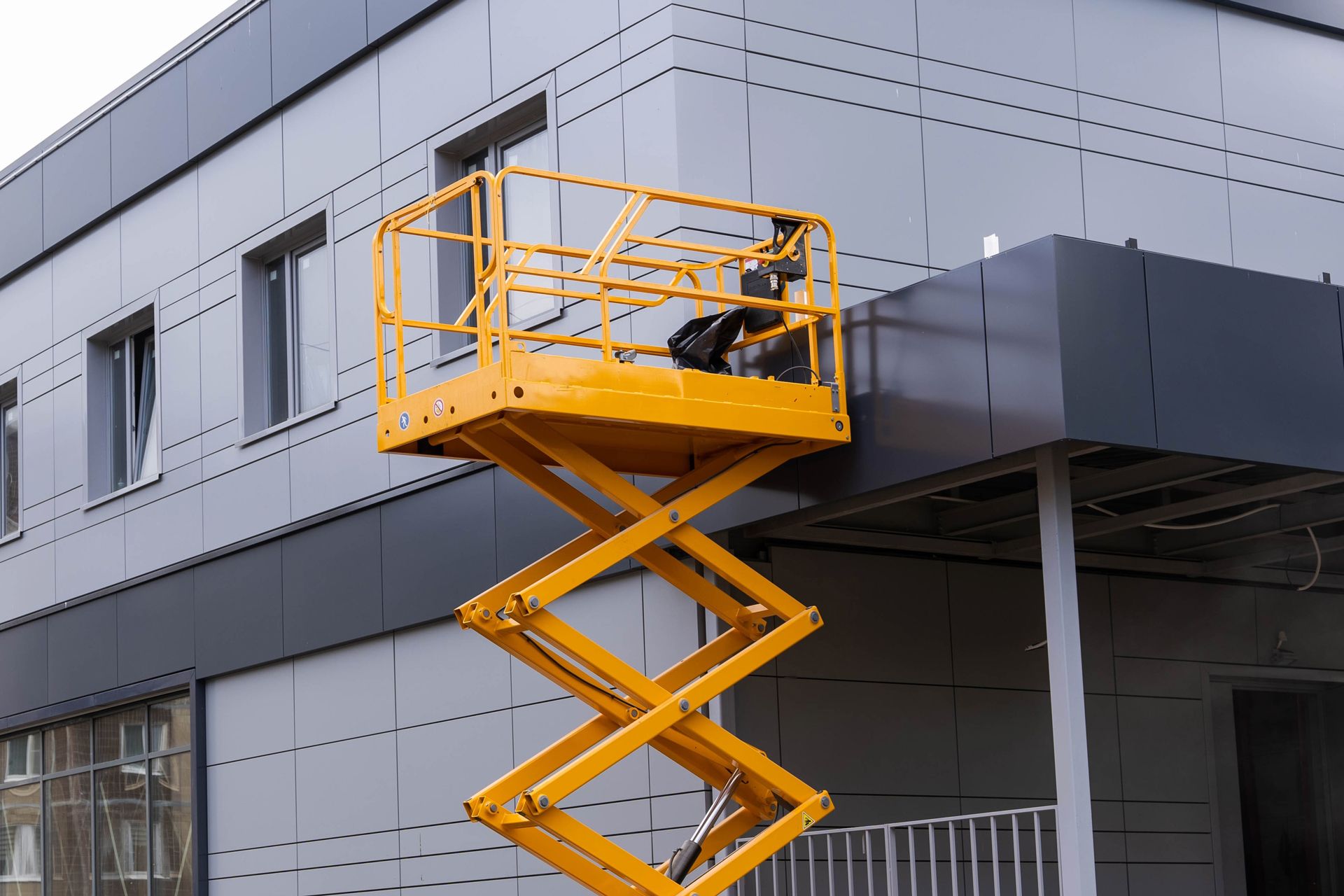 A man is standing on a scissor lift in front of a building