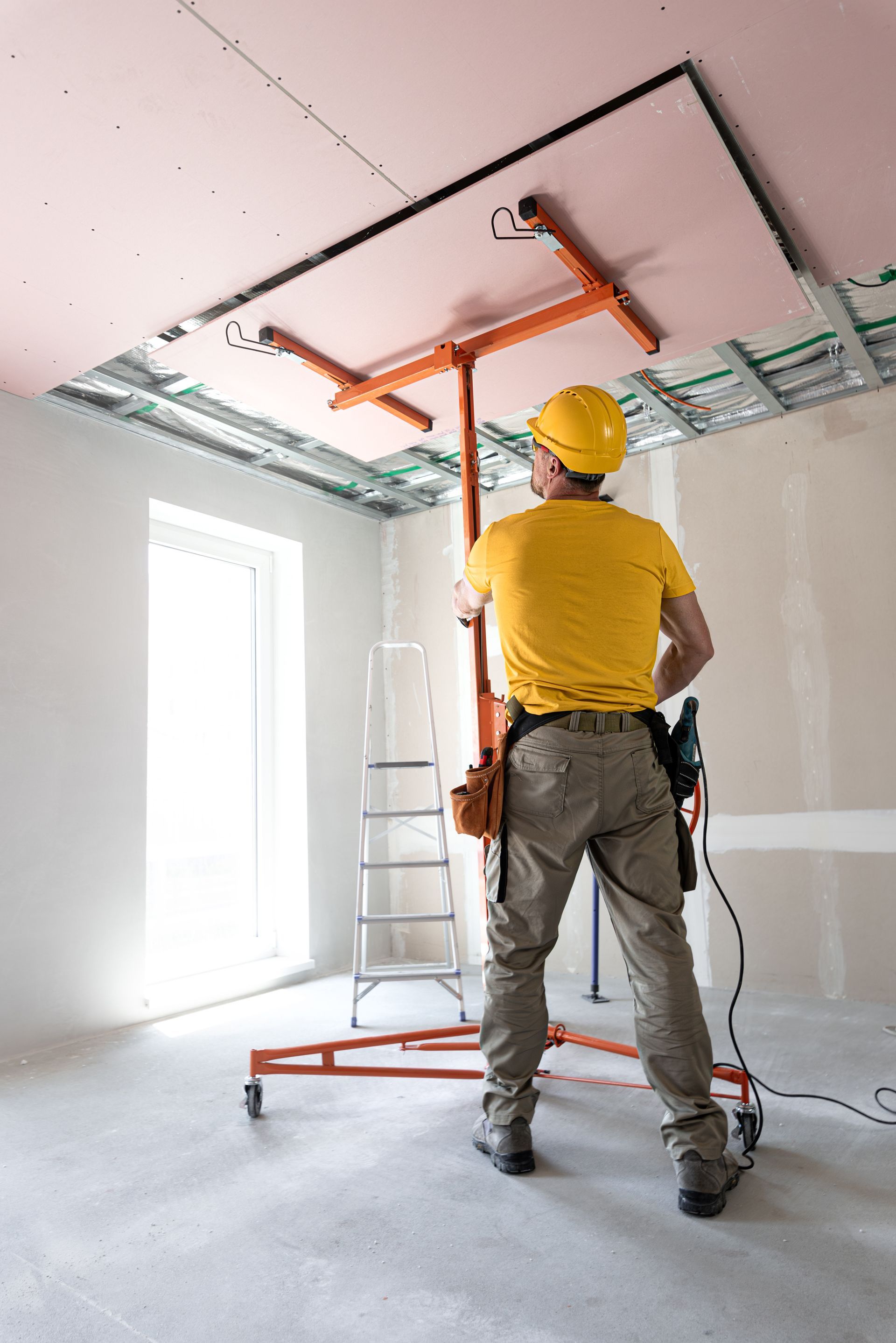 A man is standing on a ladder in a room looking up at the ceiling