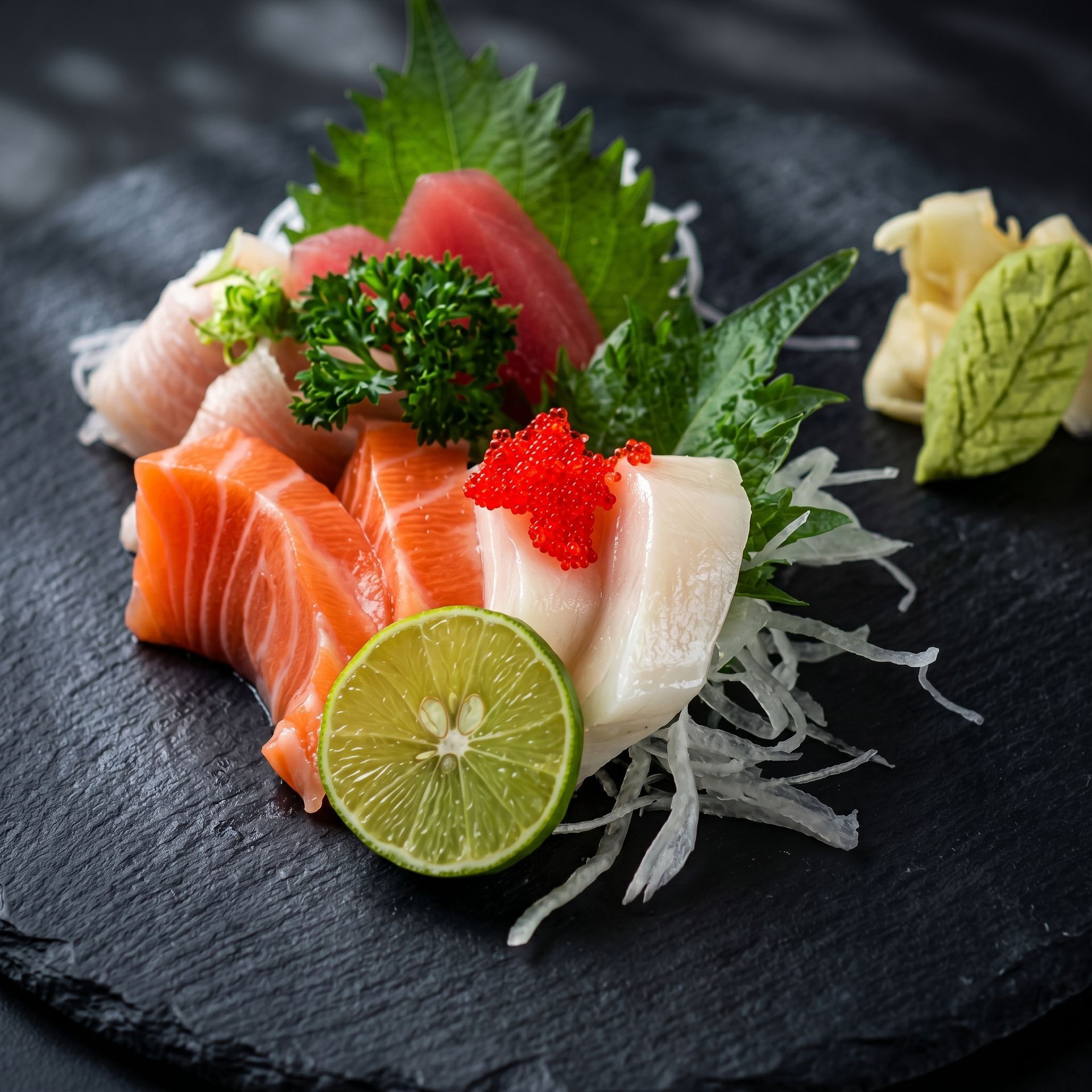 Assorted sashimi with lime and garnish on a black slate plate