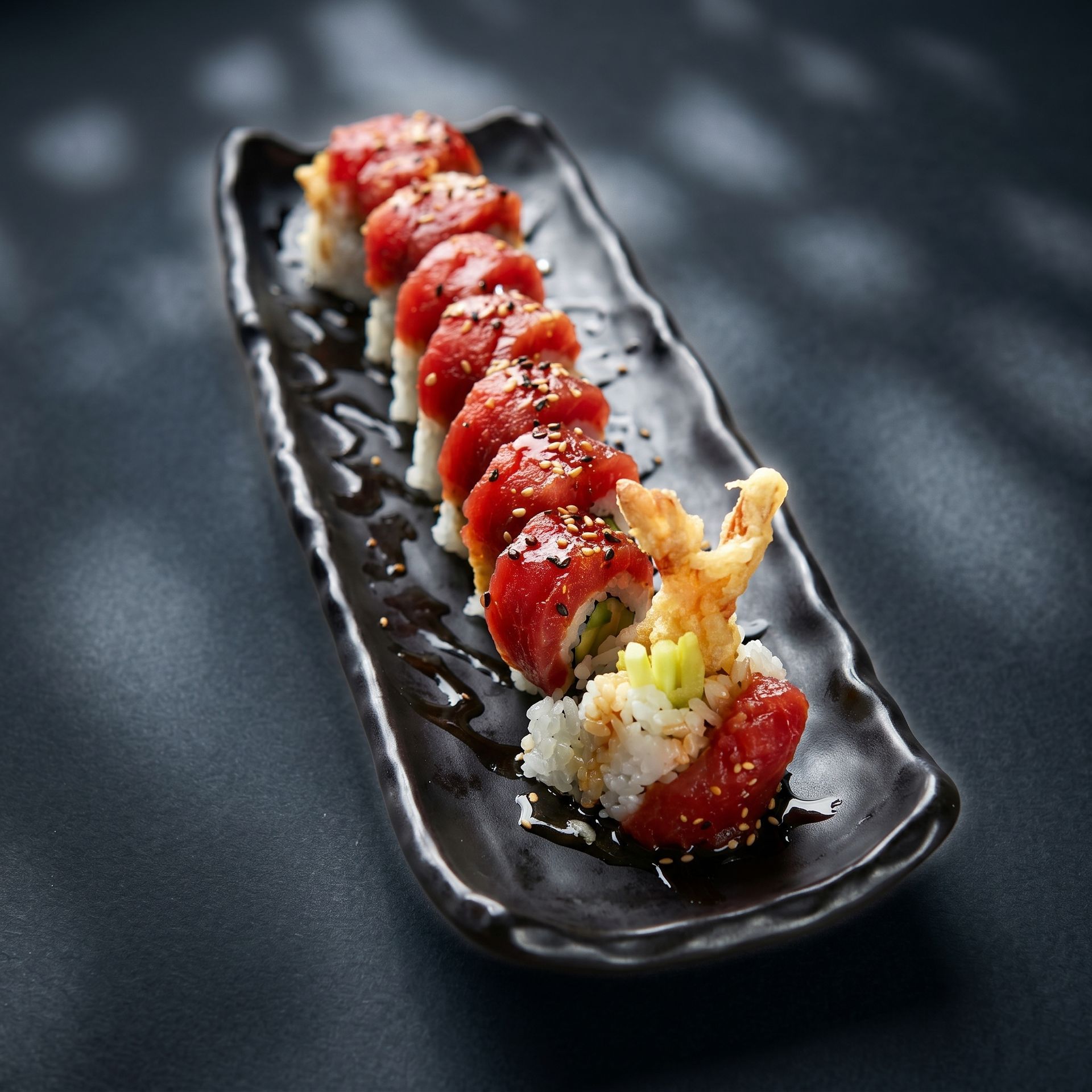 Sushi roll drizzled with red sauce on a black rectangular plate