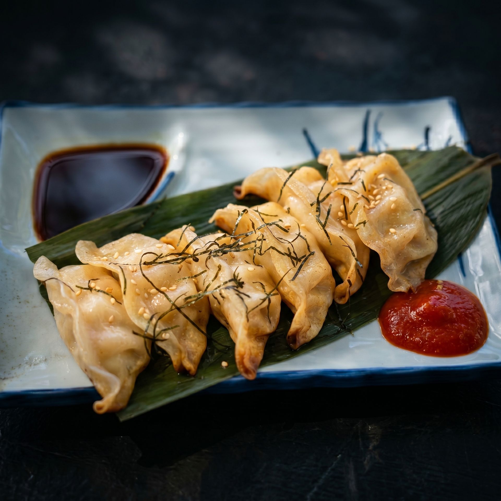 Pan-fried dumplings on a green leaf with soy sauce and red dipping sauce on a plate