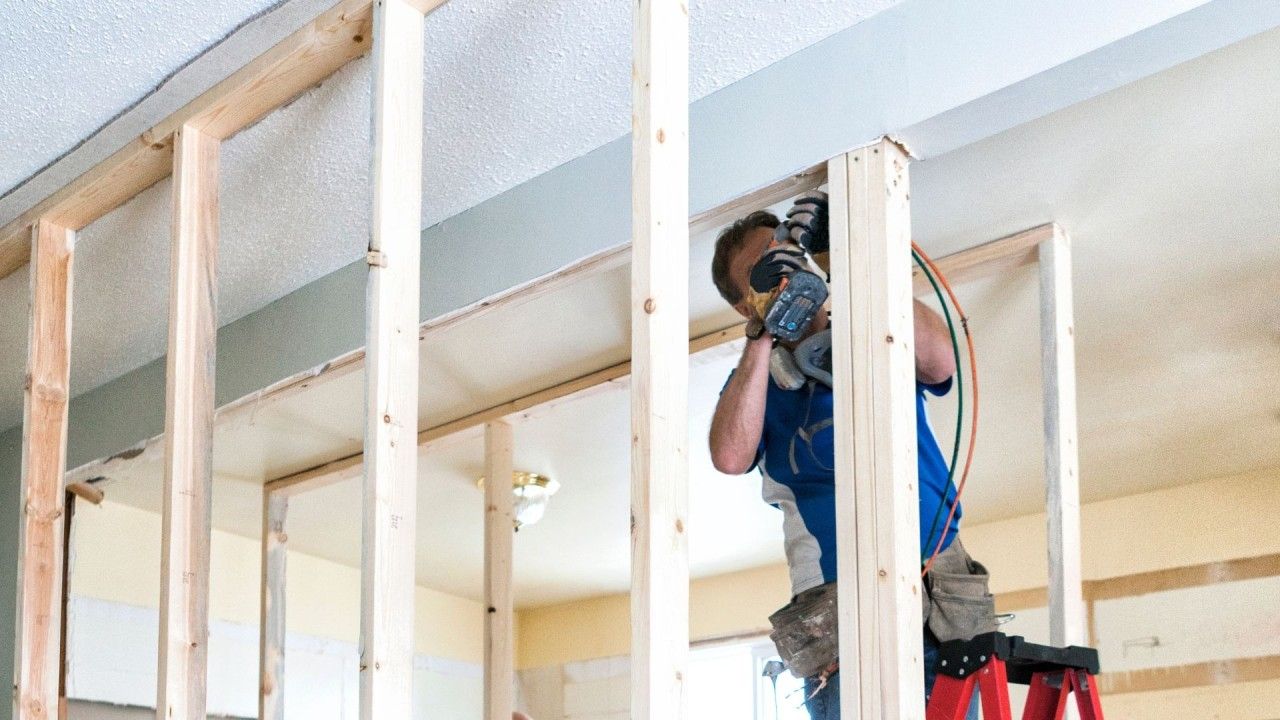 A man is standing on a ladder working on a wall.