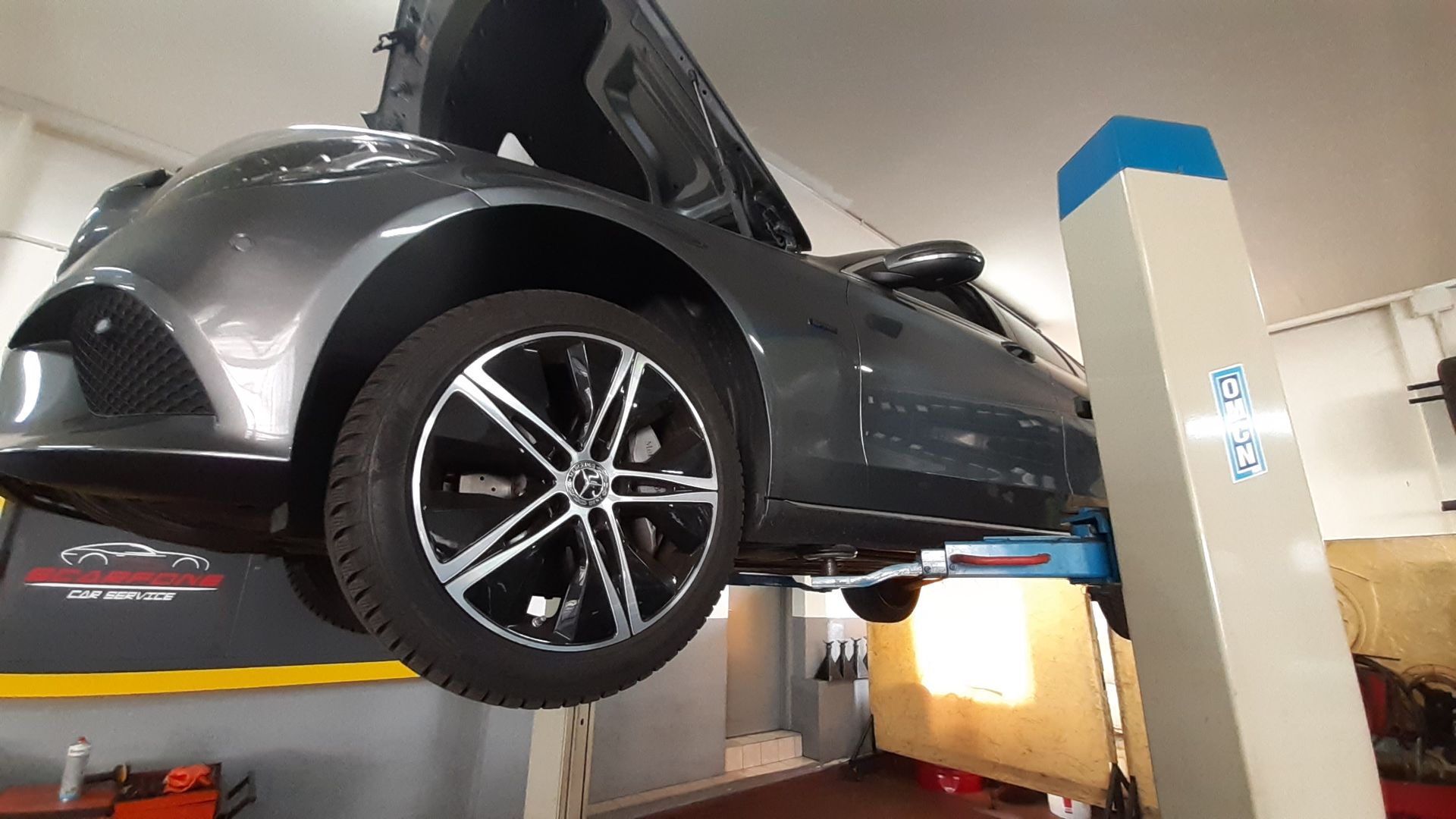 Un'auto è parcheggiata su un ponte sollevatore in un garage con il cofano alzato.