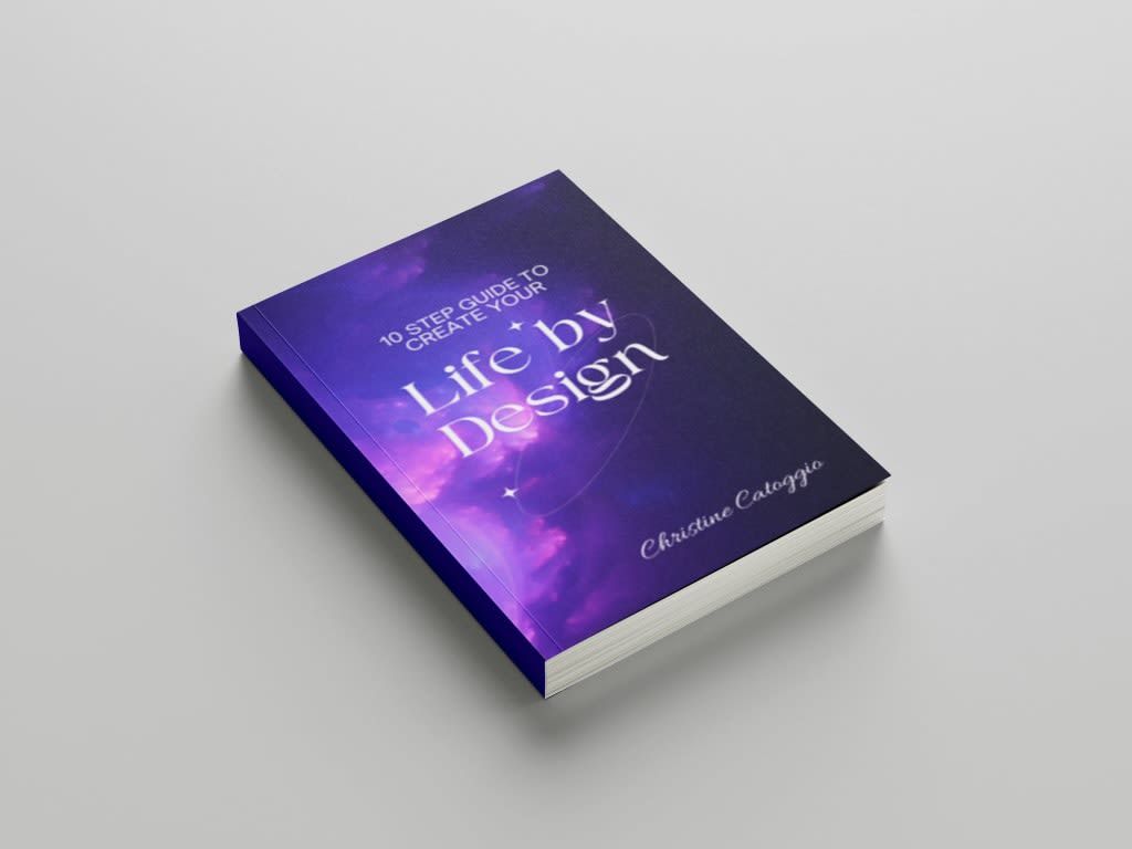 A book titled "Life by Design" with a purple and blue nebula cover, lying on a gray surface.