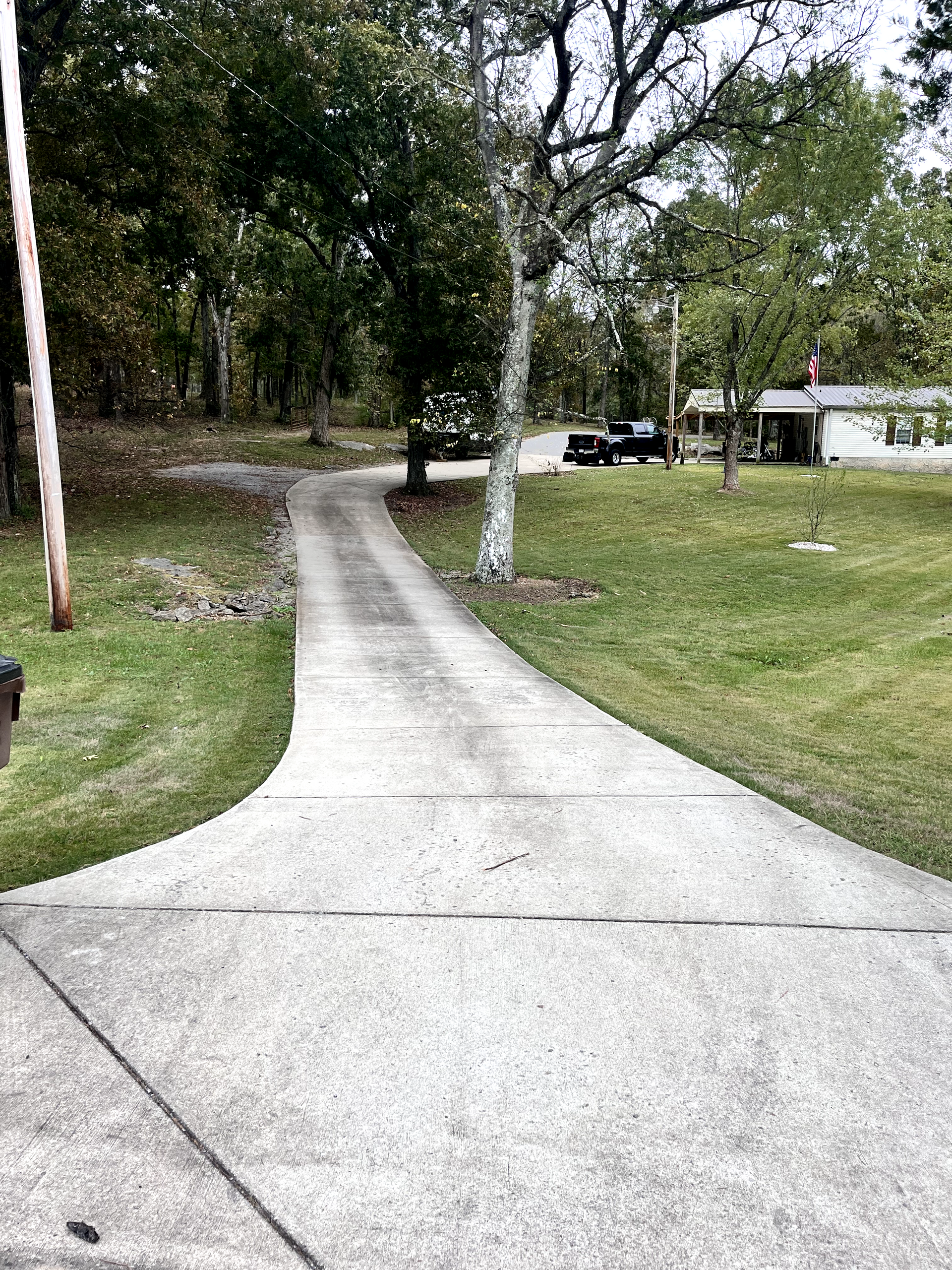 A concrete driveway leading to a house surrounded by trees and grass.