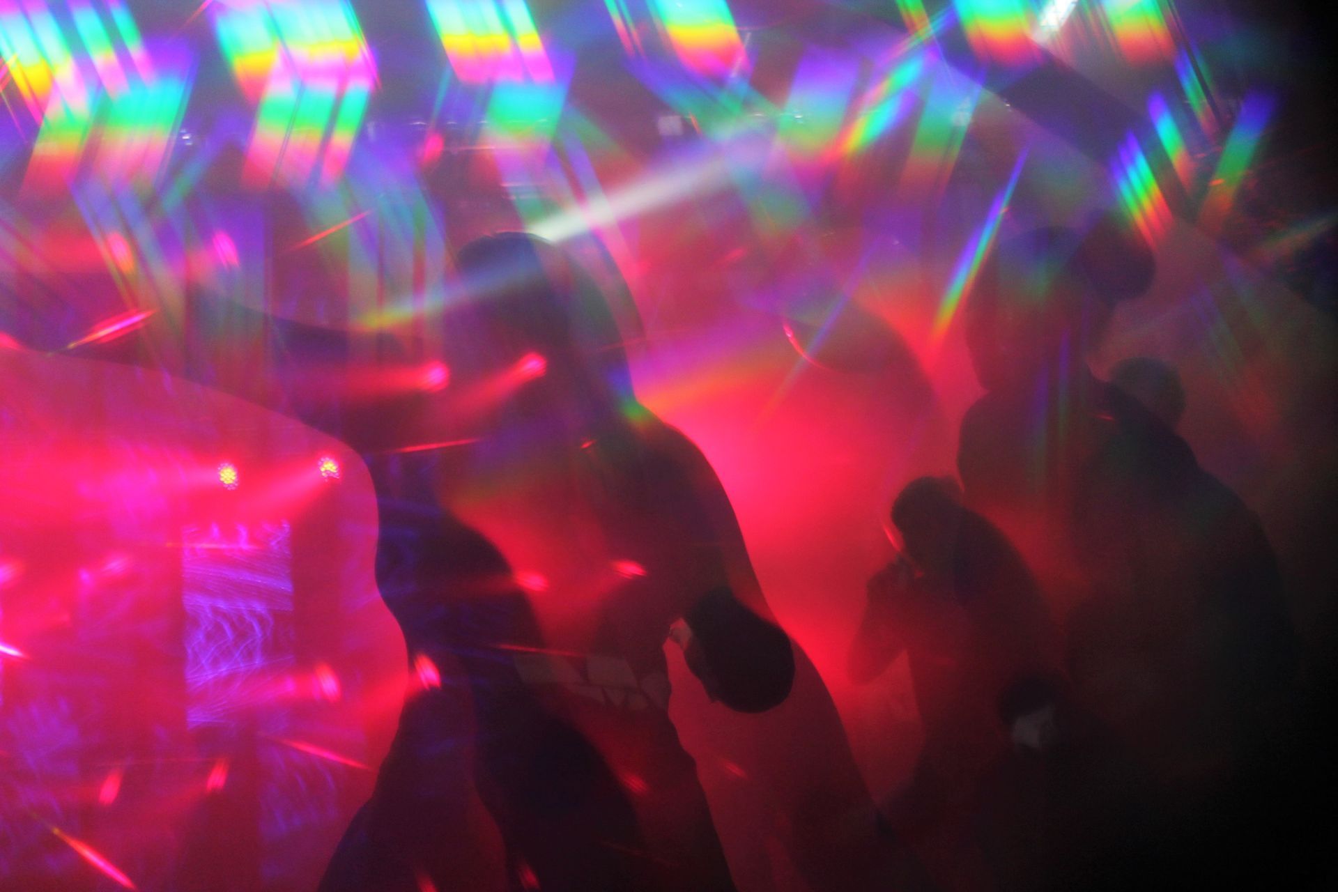 People silhouetted in a club with colorful light flares and pink/red lighting.