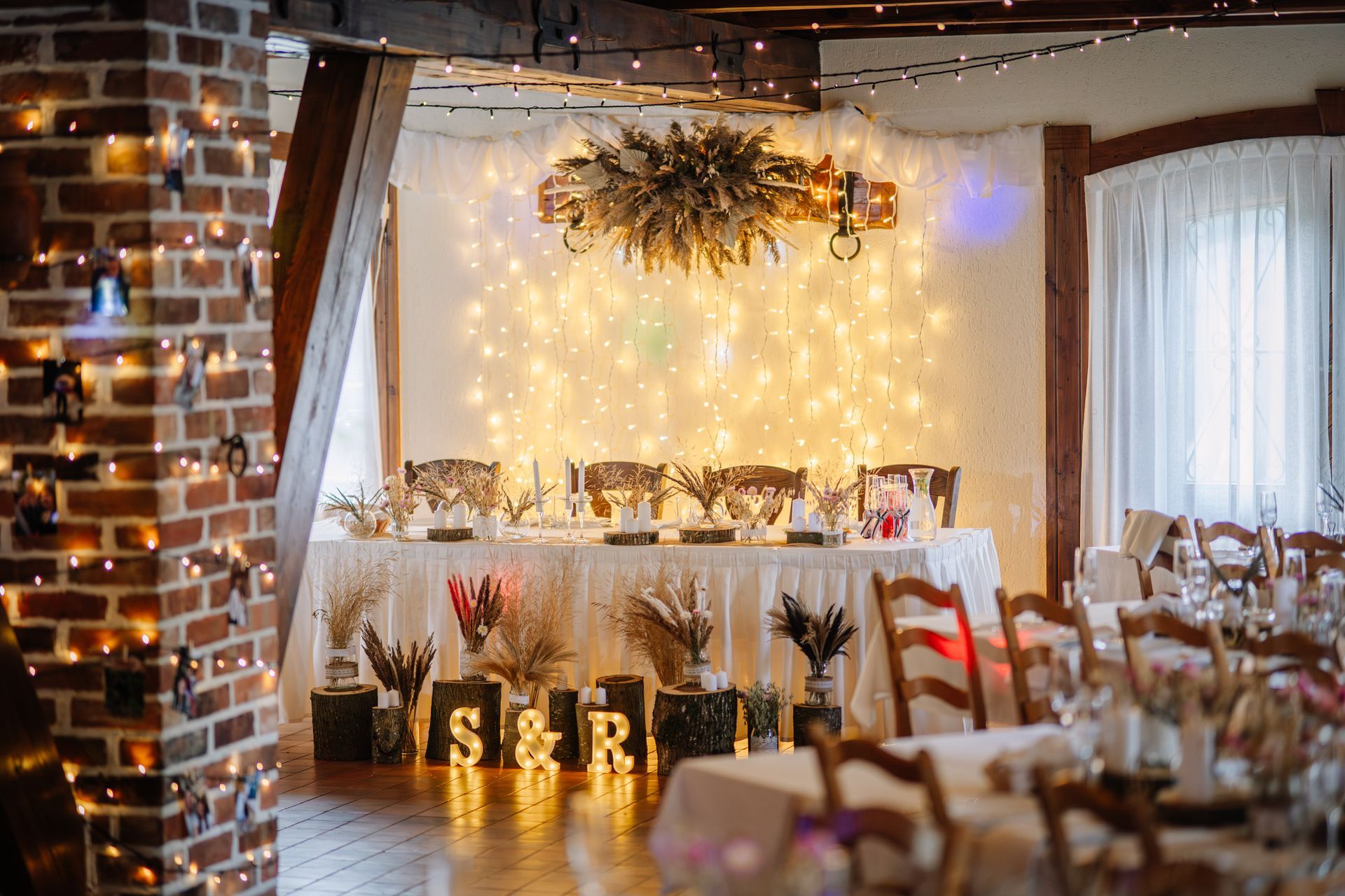 Wedding reception decorated with fairy lights and floral arrangements. Table setting with S&R initials.
