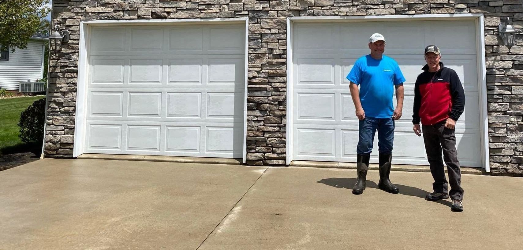 Two men are standing in front of a garage door.