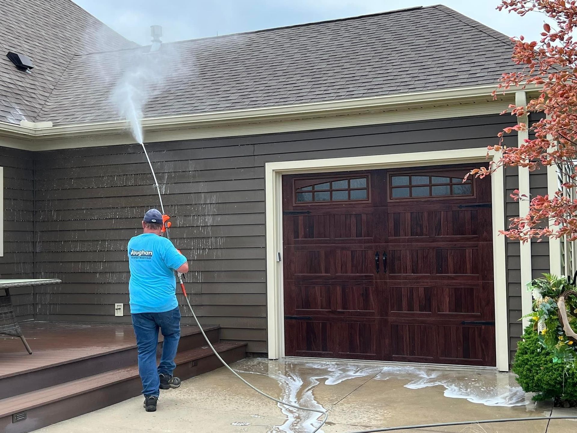 A man is cleaning the roof of a house with a pressure washer.
