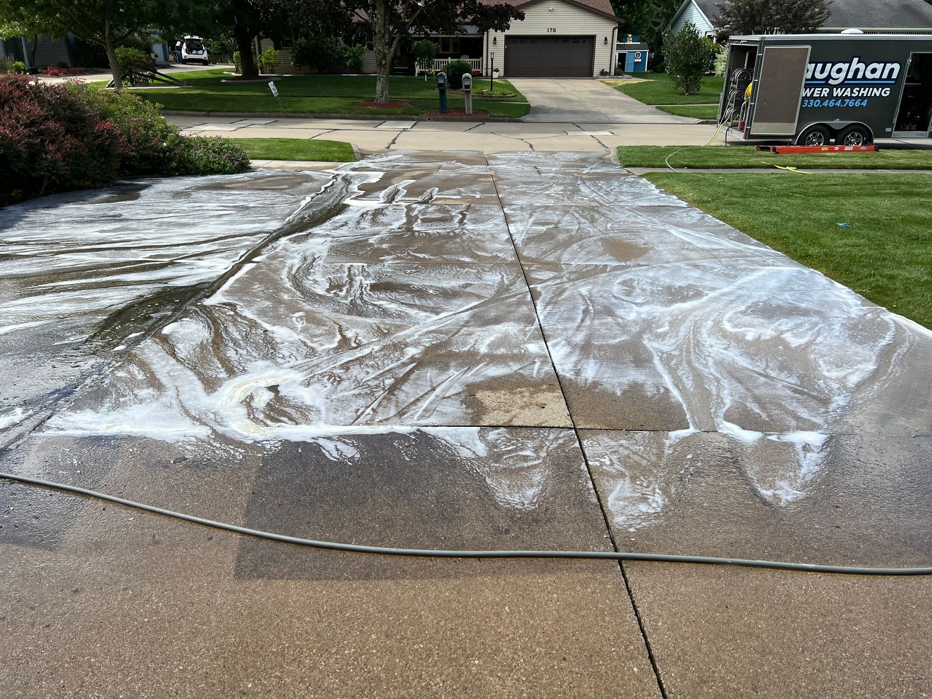 A concrete driveway is being cleaned with a hose.