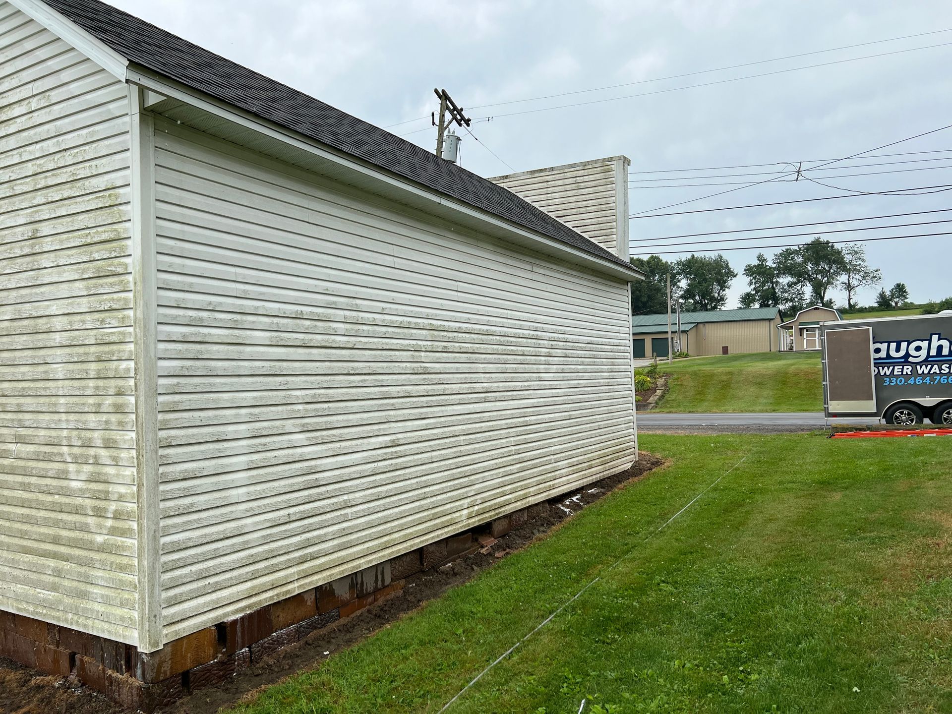 A white building with a black roof is sitting in the middle of a grassy field.