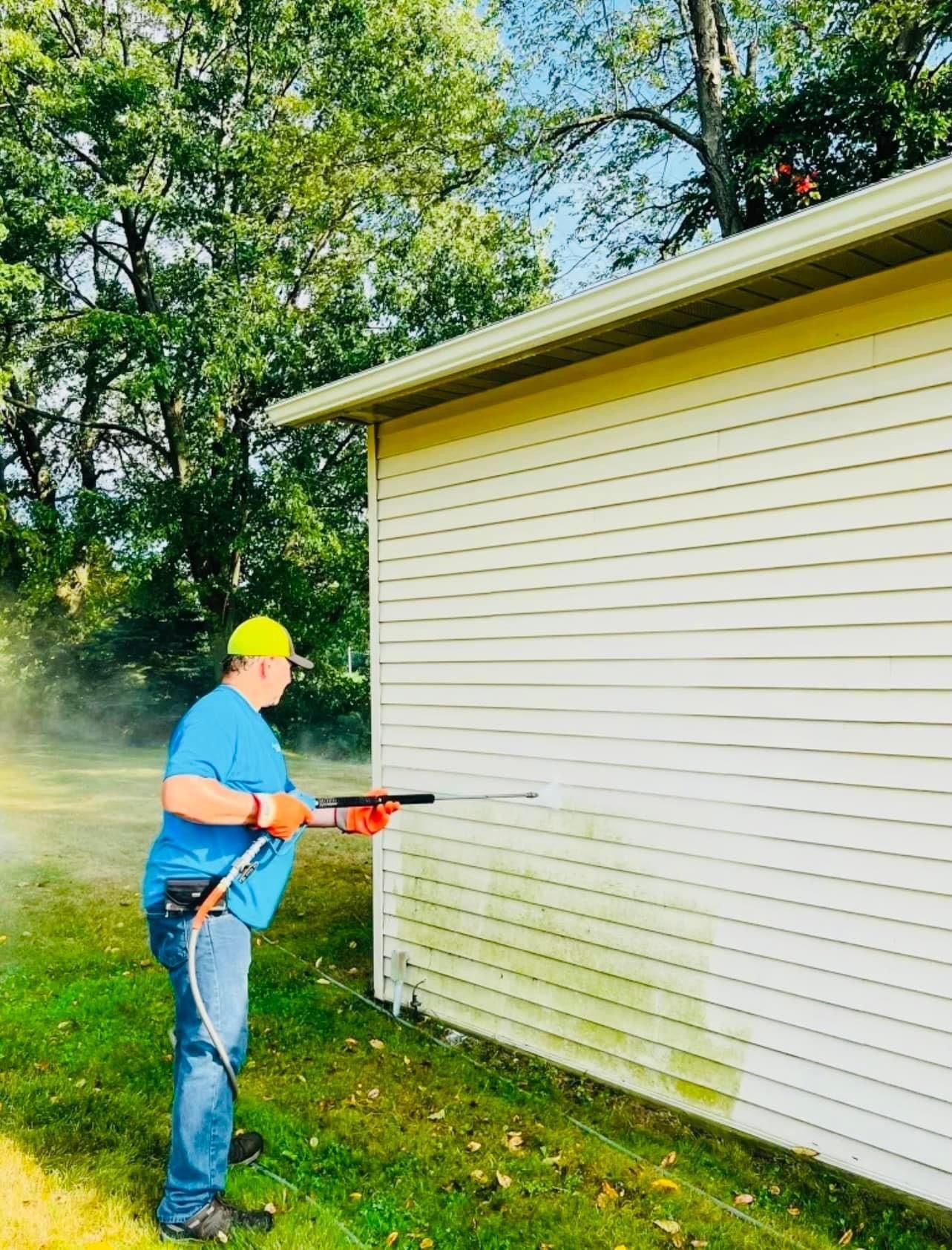 A man is cleaning the side of a house with a pressure washer.