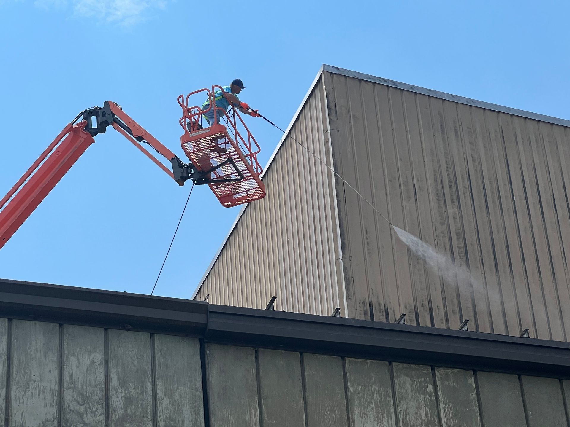 A man is cleaning the side of a building with a high pressure washer.
