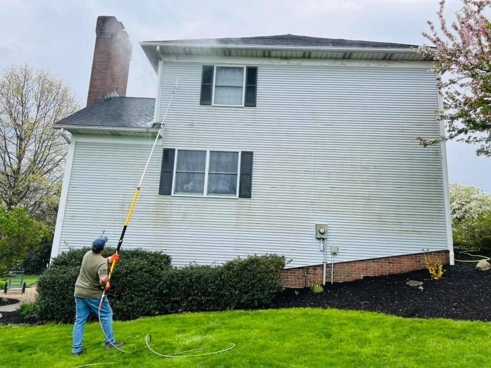 A man is cleaning the side of a white house with a pressure washer.