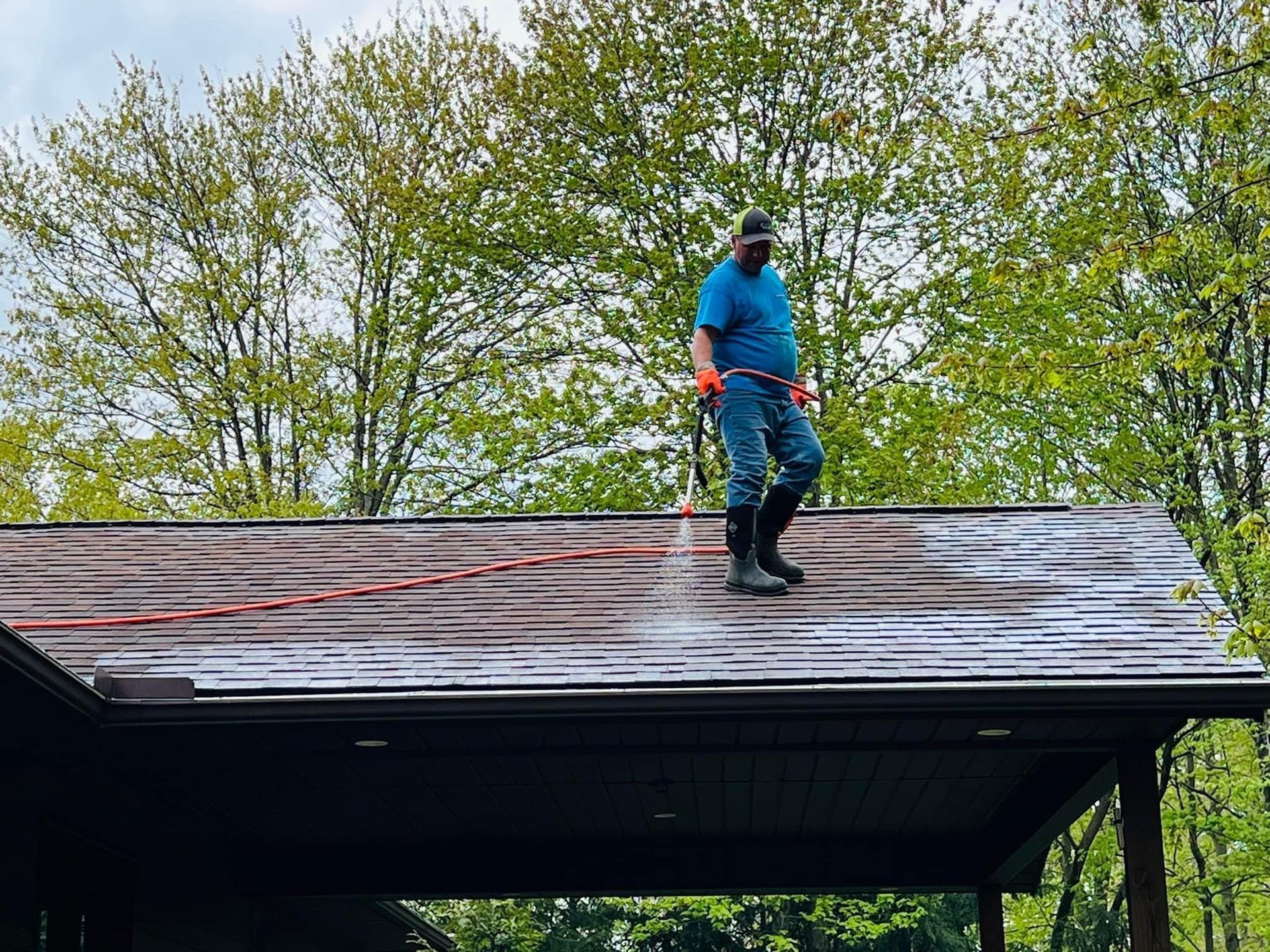 A man is standing on top of a roof spraying water on it.