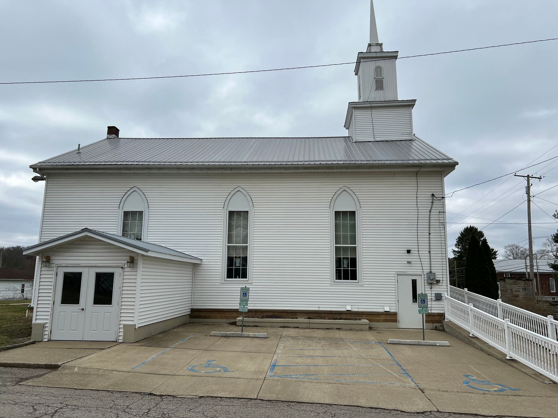 A white church with a steeple and a white fence in front of it.