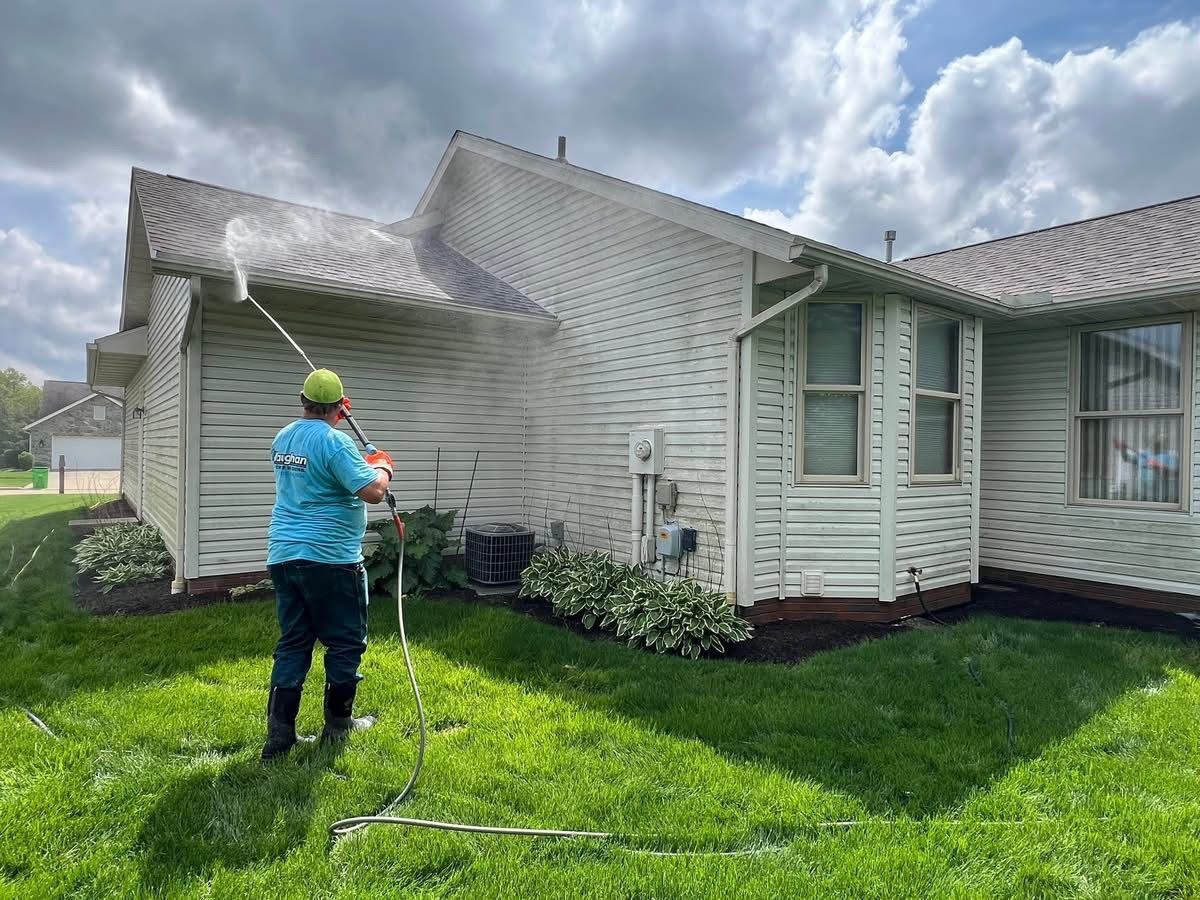 A man is cleaning the side of a house with a pressure washer.