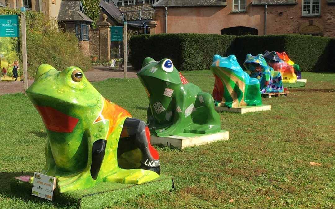 A row of colorful toad statues are sitting in the grass, part of Taunton Toads.