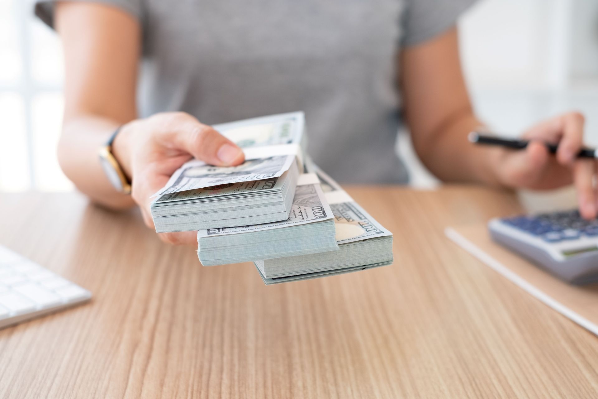 Close-up of a woman’s hand as she holds wads of dollars to the camera as she sits on a table. Close-up of a woman’s hand as she holds wads of dollars to the camera as she sits on a table.