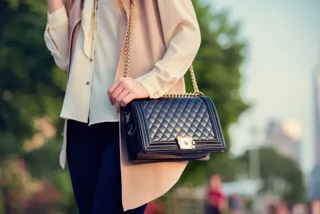 A woman is holding a black purse on a chain.