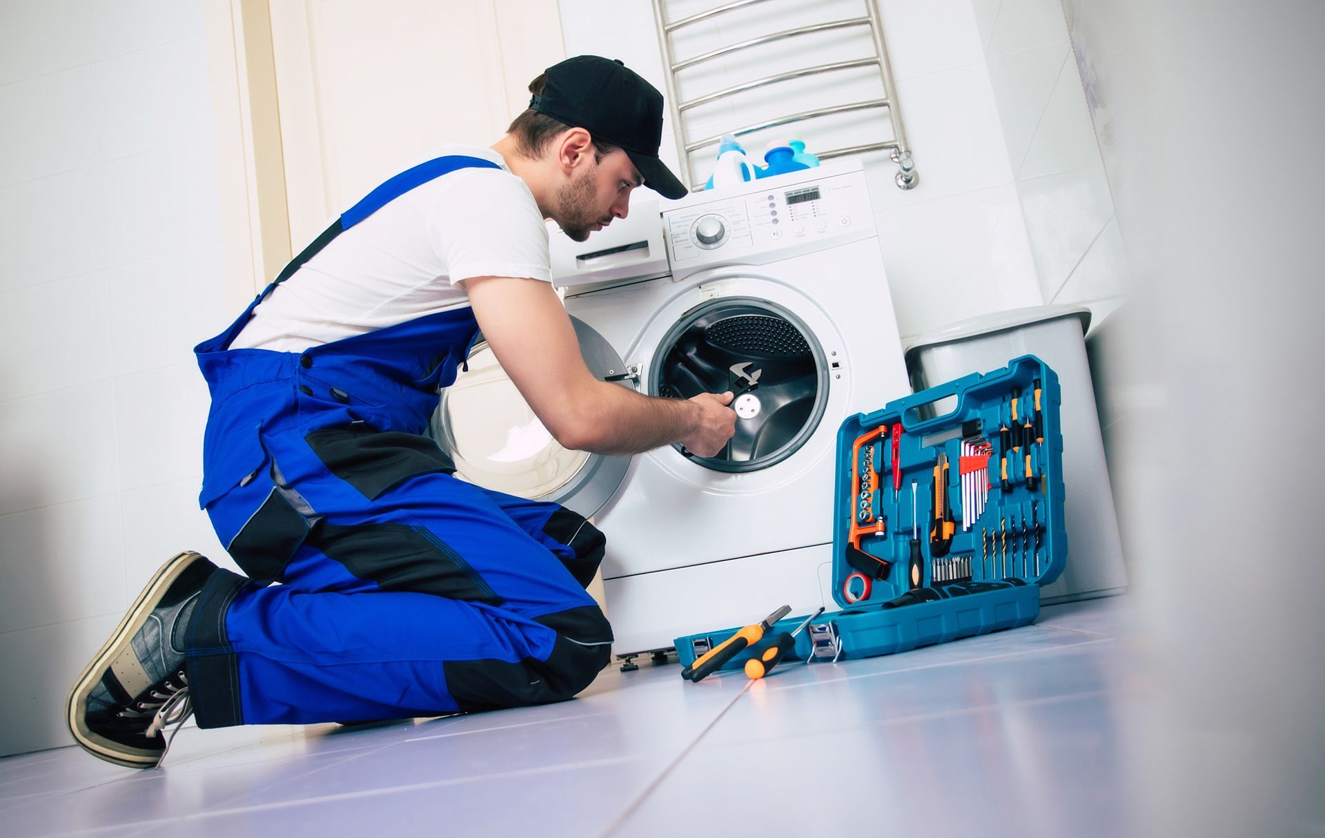 A man is kneeling down fixing a washing machine.