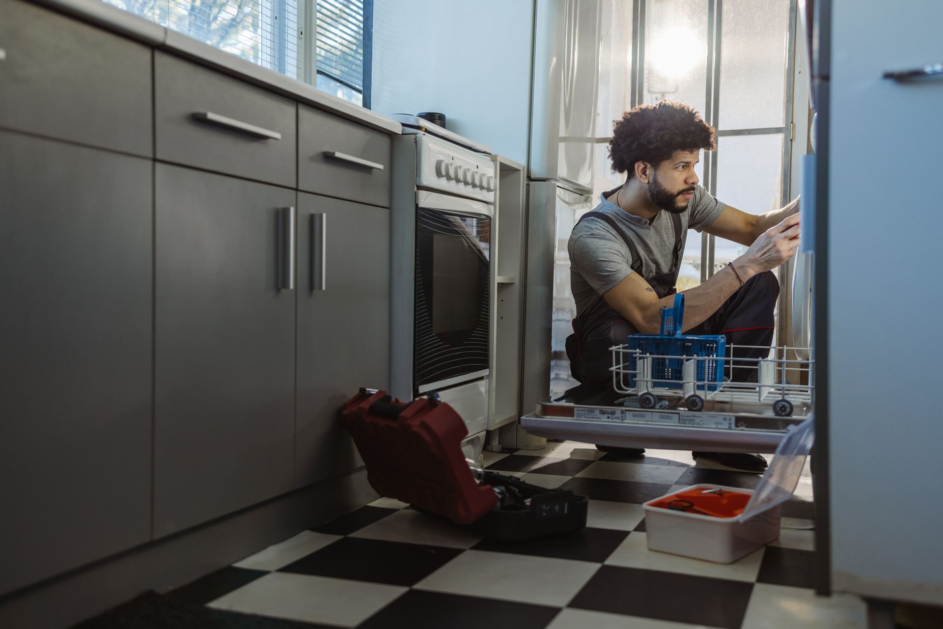 A man is kneeling down in a kitchen fixing a refrigerator.