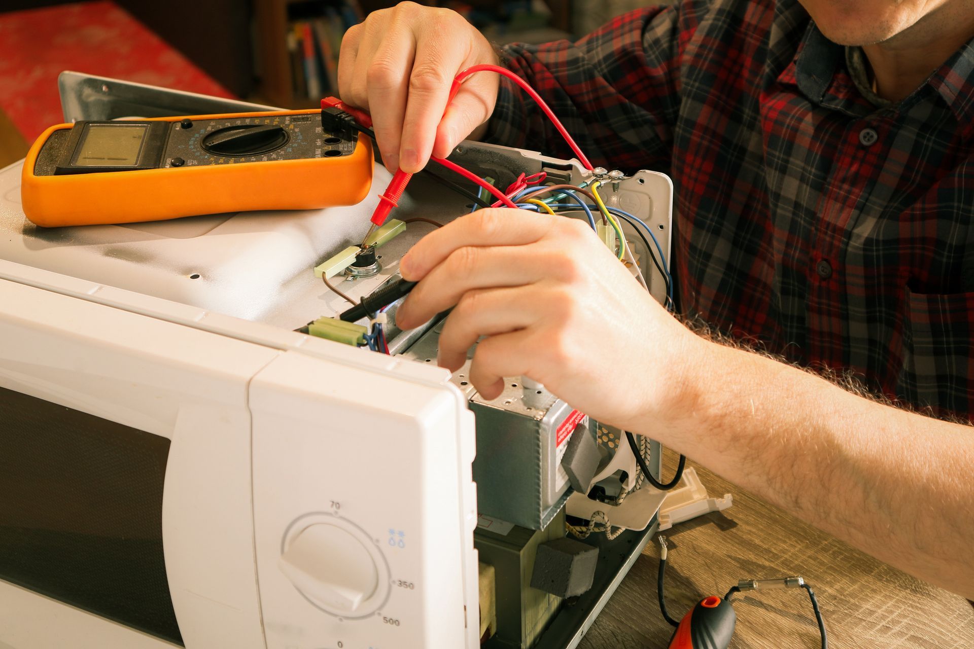 A man is fixing a microwave with a multimeter.