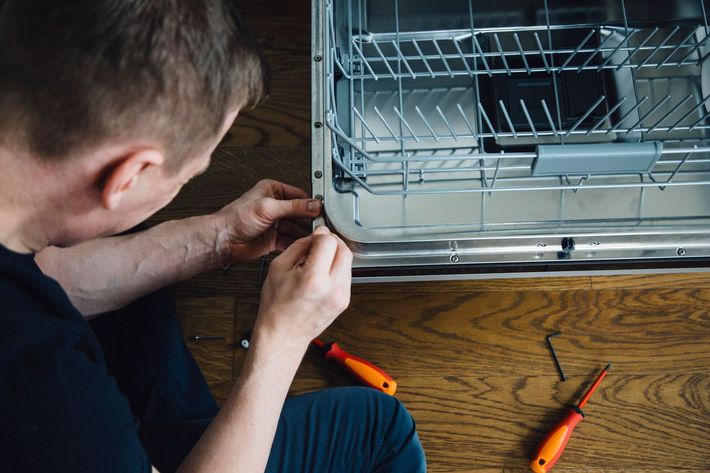 A man is fixing a washing machine in a kitchen. A man is fixing a washing machine in a kitchen.