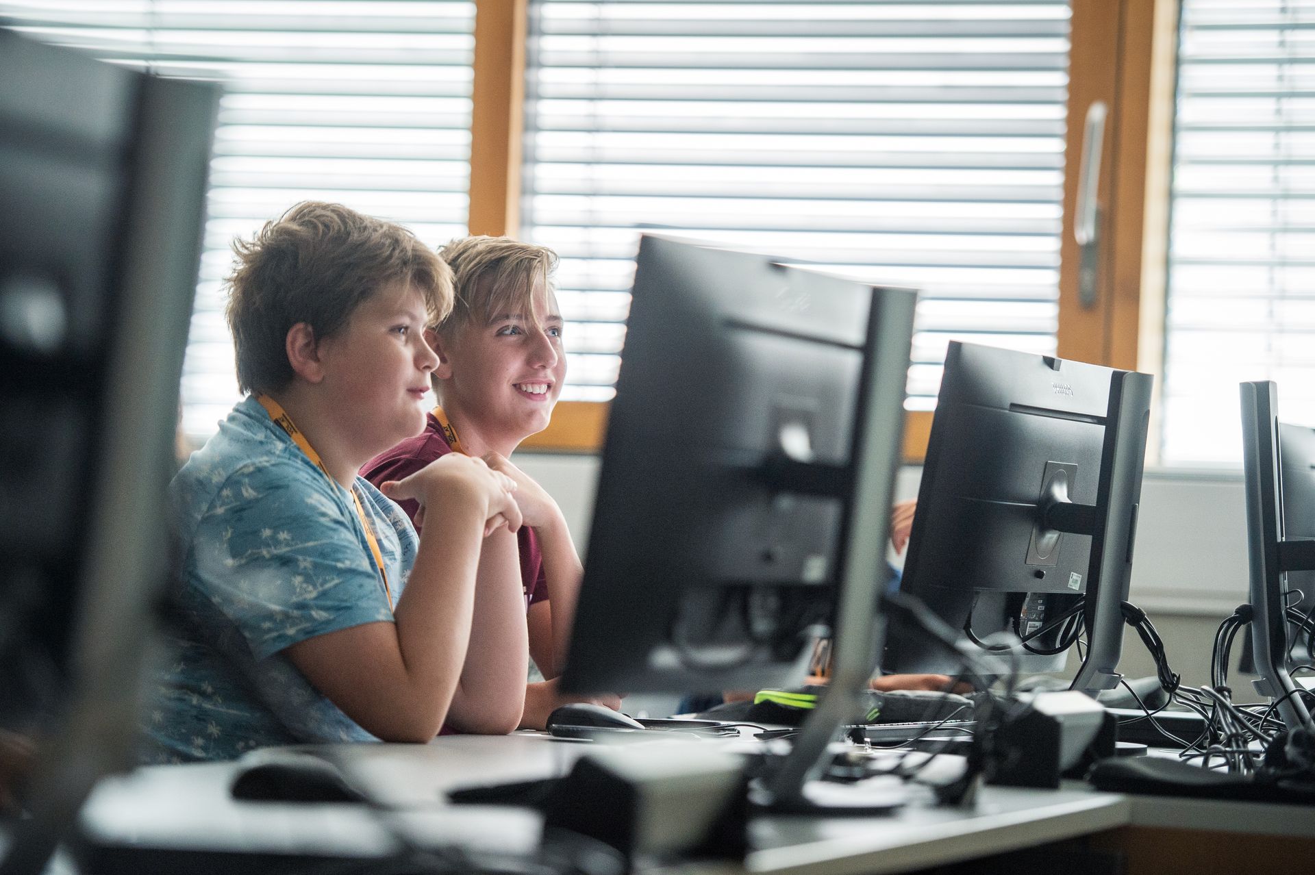 Zwei Kiner sitzen in einem Klassenzimmer vor Computerbildschirmen.