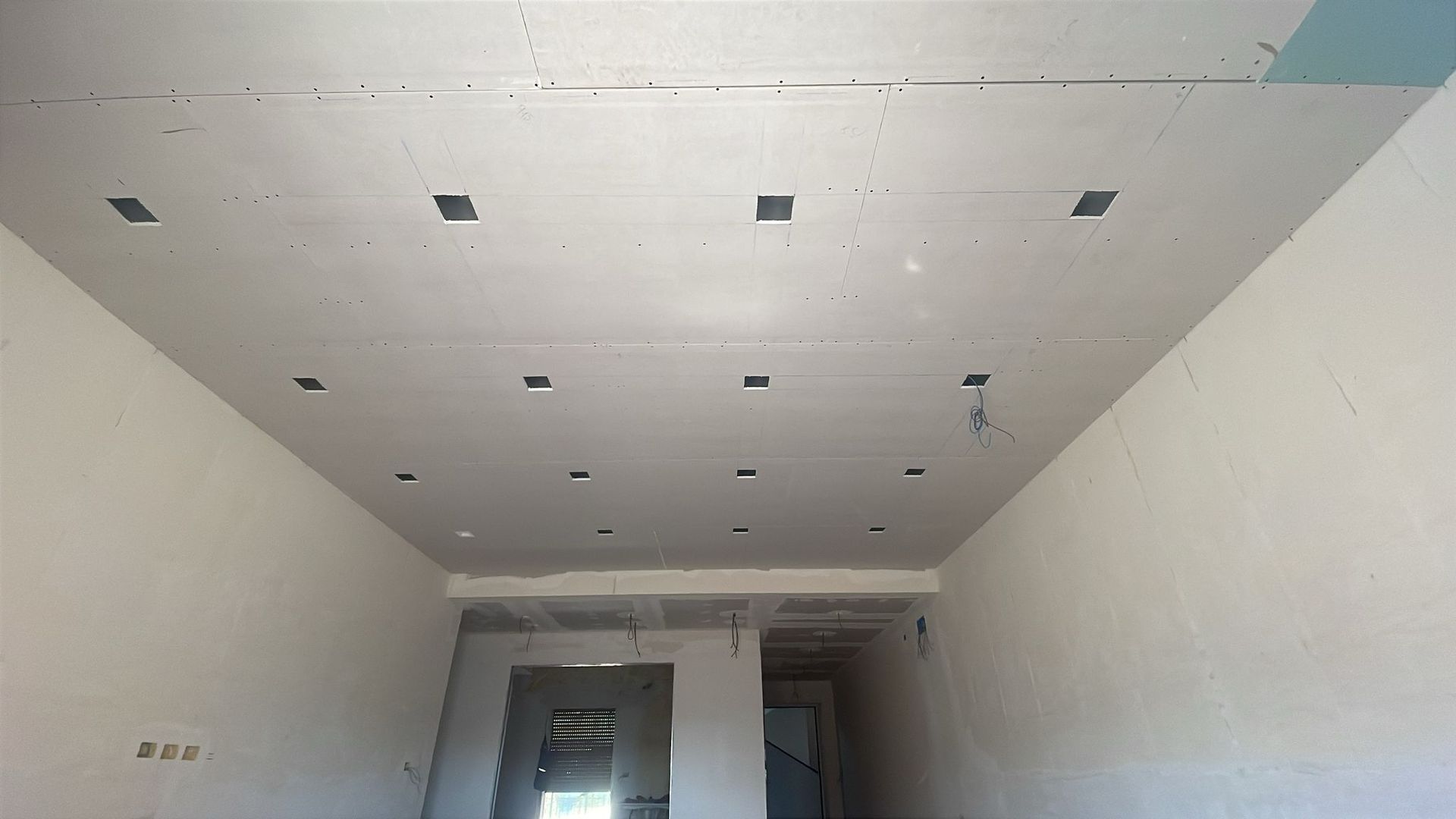 Stanza con pareti e soffitto bianchi grezzi. Il soffitto presenta fori quadrati per l'illuminazione a incasso.