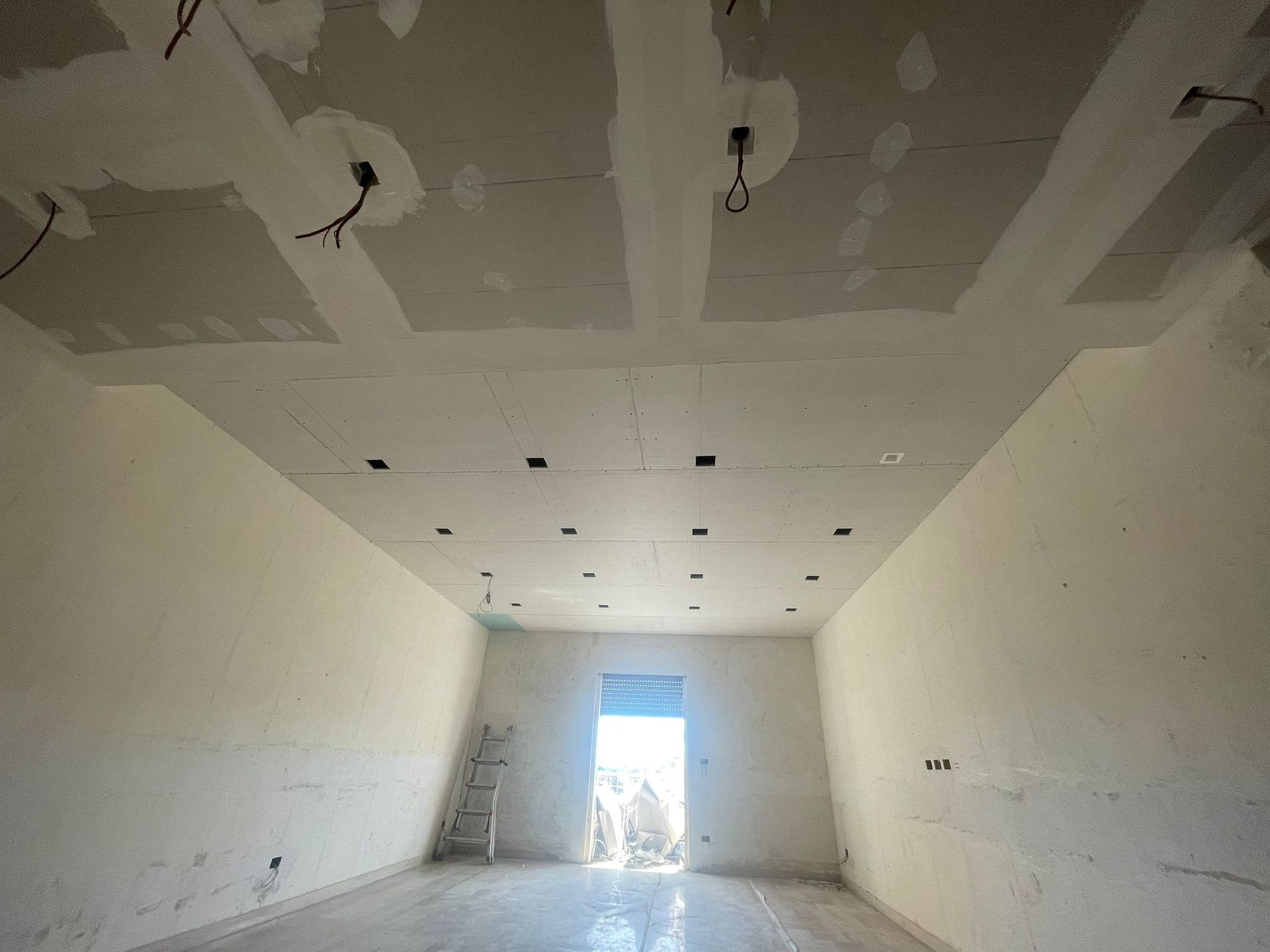 Stanza grezza con soffitto, pareti e porta in cartongesso. Scala al centro, fili elettrici penzolanti.