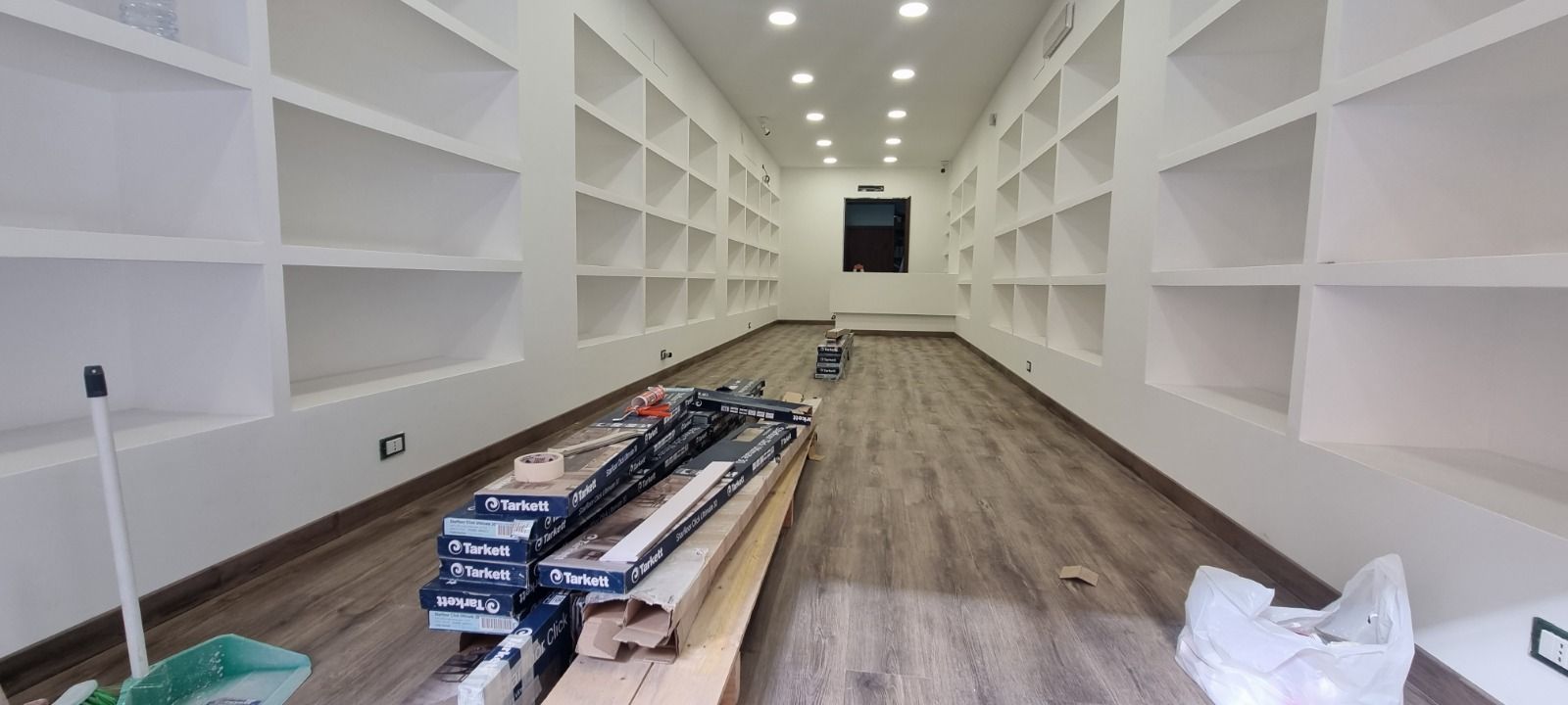 Interno di una stanza con scaffali bianchi integrati su entrambi i lati, pavimento in legno e materiali da costruzione.