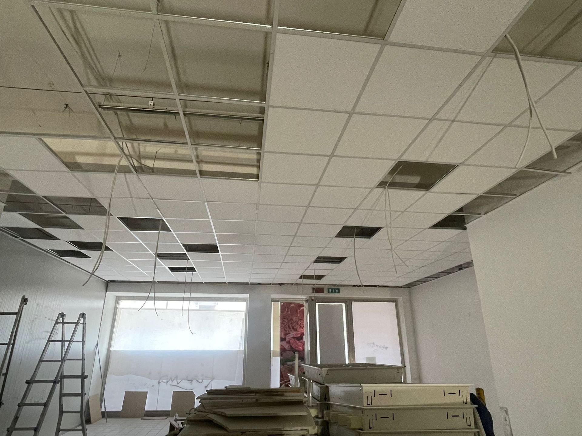 Pannelli del soffitto installati in una stanza con fili elettrici scoperti e una scala.