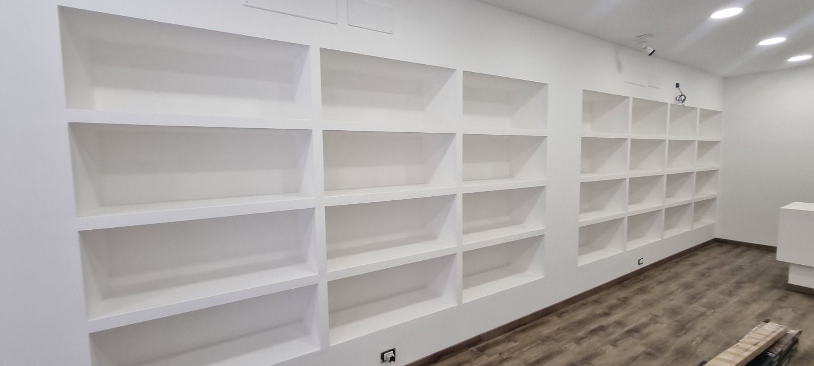 Scaffali bianchi a muro in un moderno spazio commerciale. Pavimento marrone e pareti bianche.