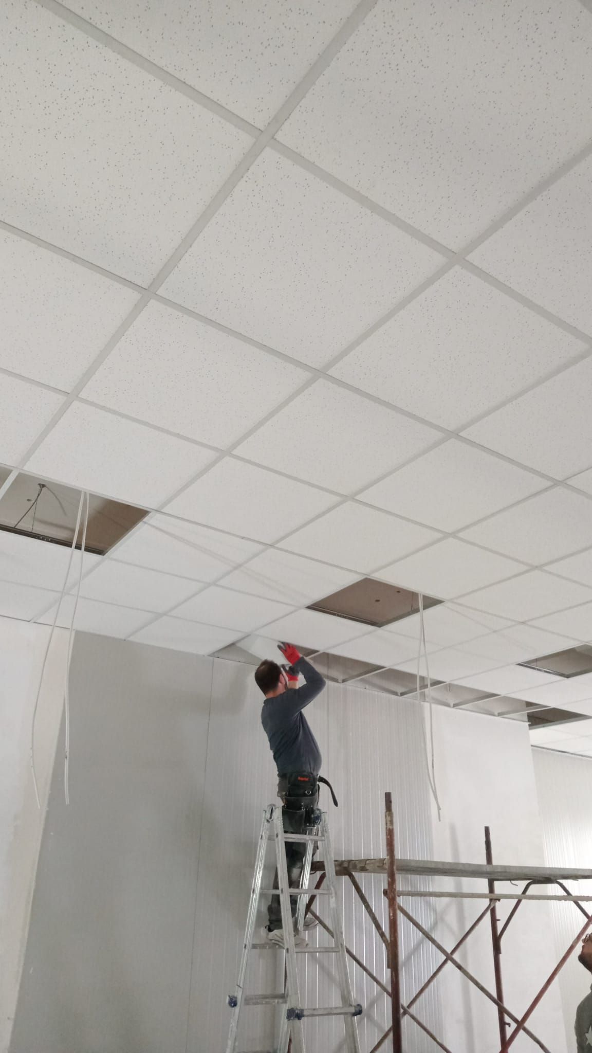 Persona su una scala che installa un pannello del controsoffitto in una stanza in costruzione.