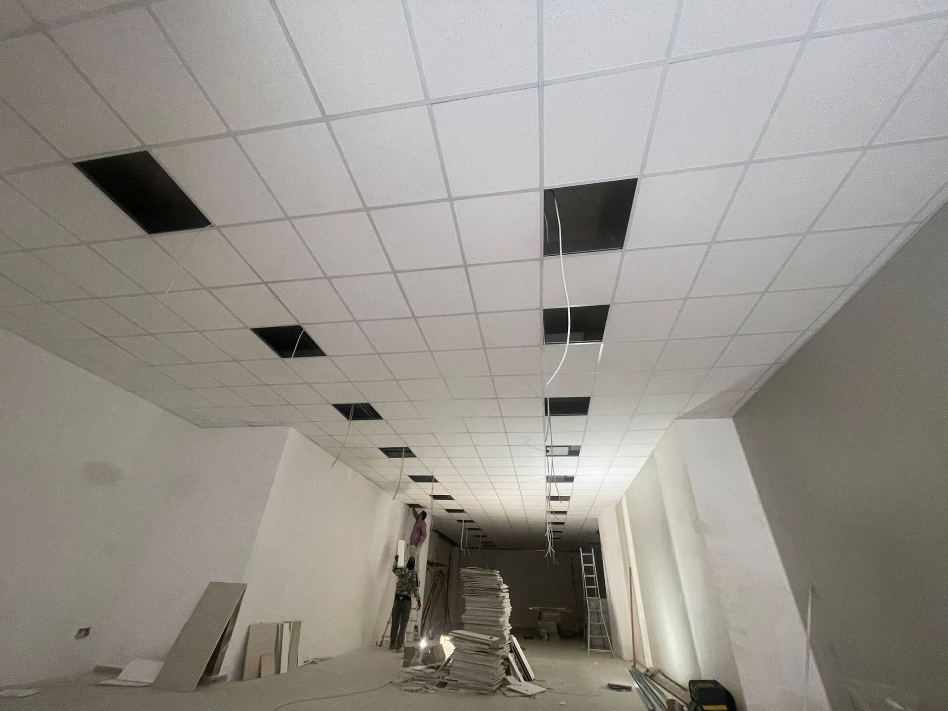Vista interna di un cantiere con soffitto a griglia, rettangoli aperti e pareti bianche spoglie.
