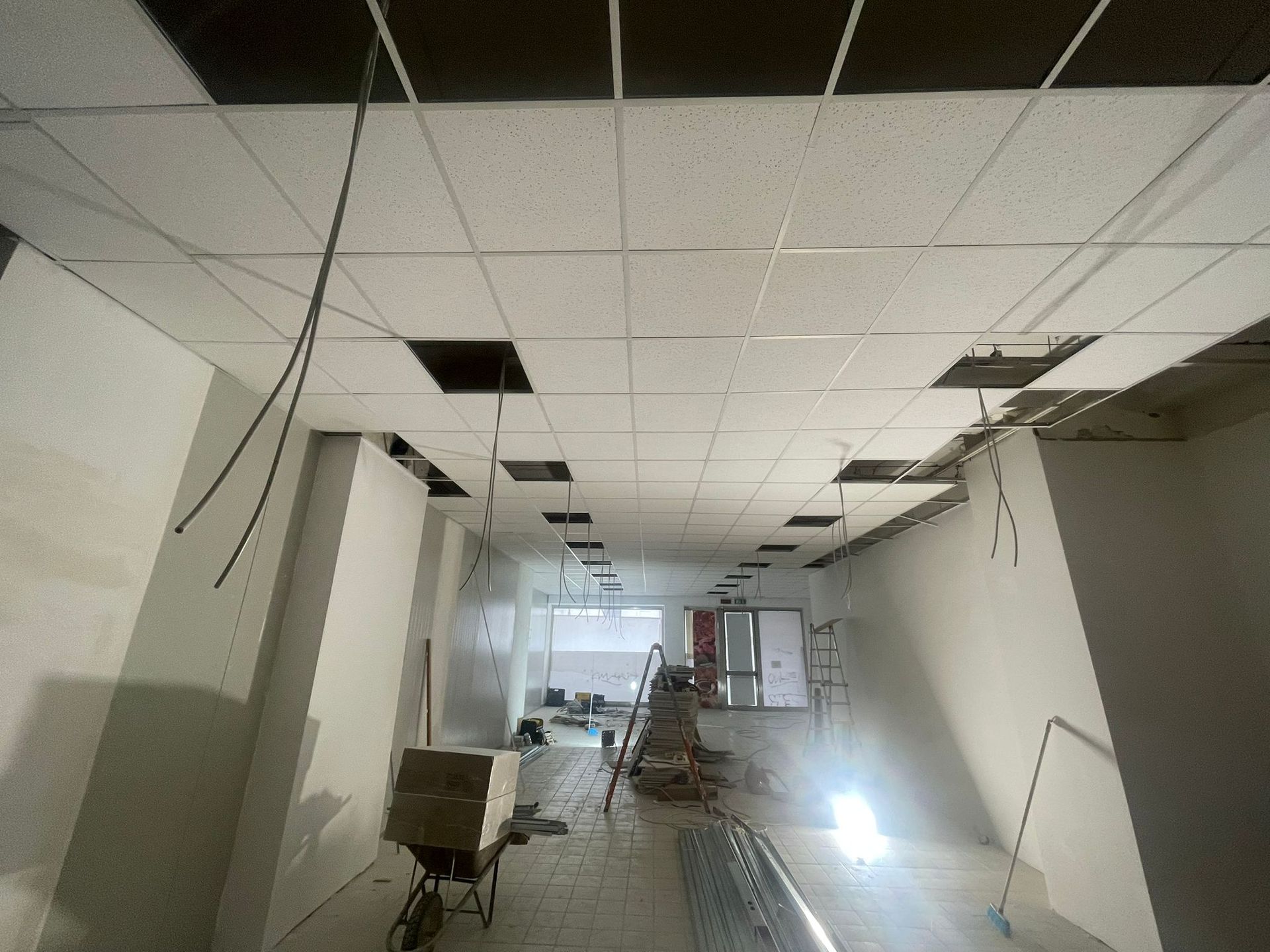Cantiere di costruzione interno; controsoffitto parzialmente installato, cavi elettrici esposti.