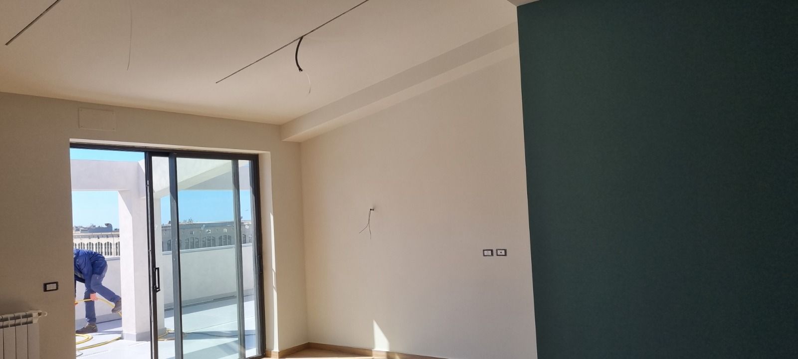 Interno di una stanza con pareti bianche, una parete decorativa blu scuro e una porta scorrevole in vetro.