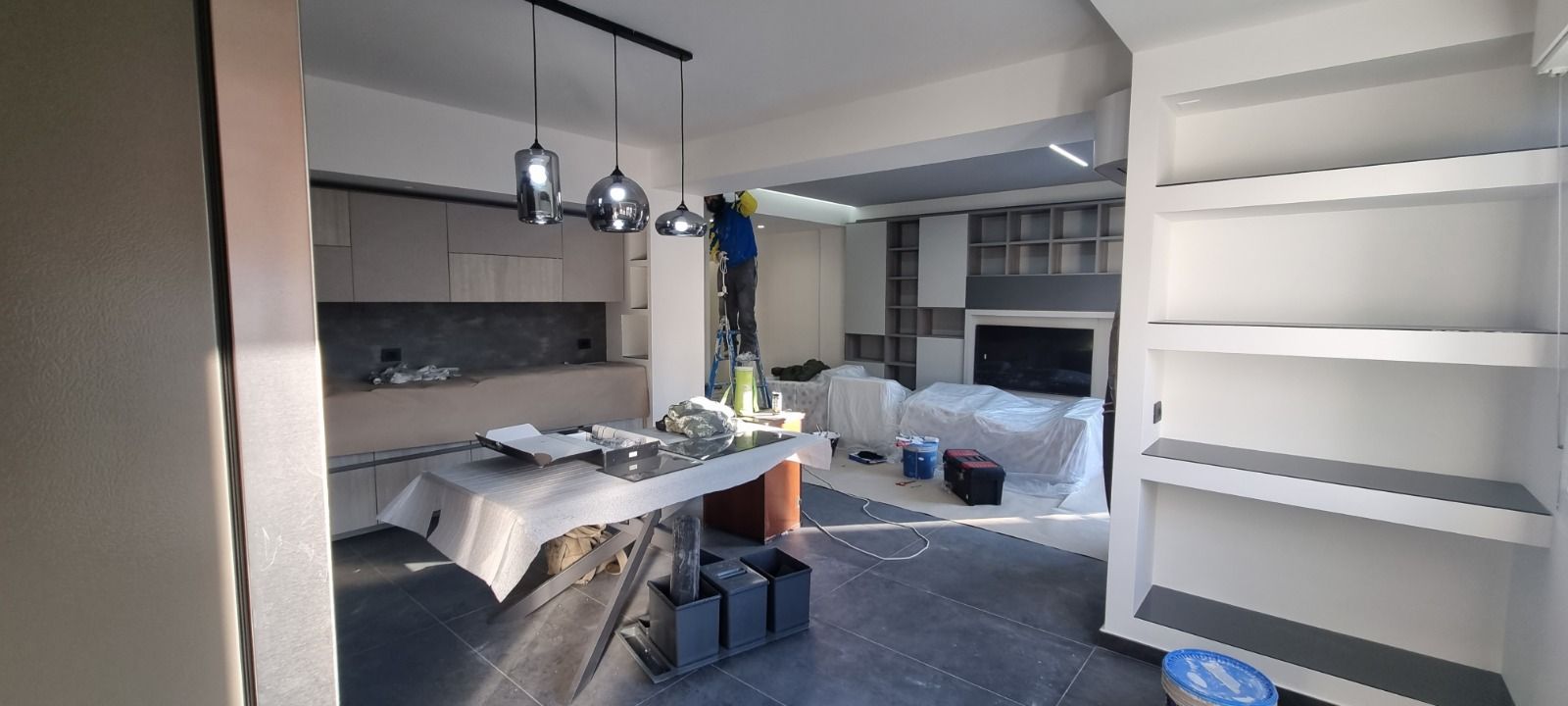 Interno di una stanza in costruzione, con un tavolo, mobili da cucina e una scaffalatura.