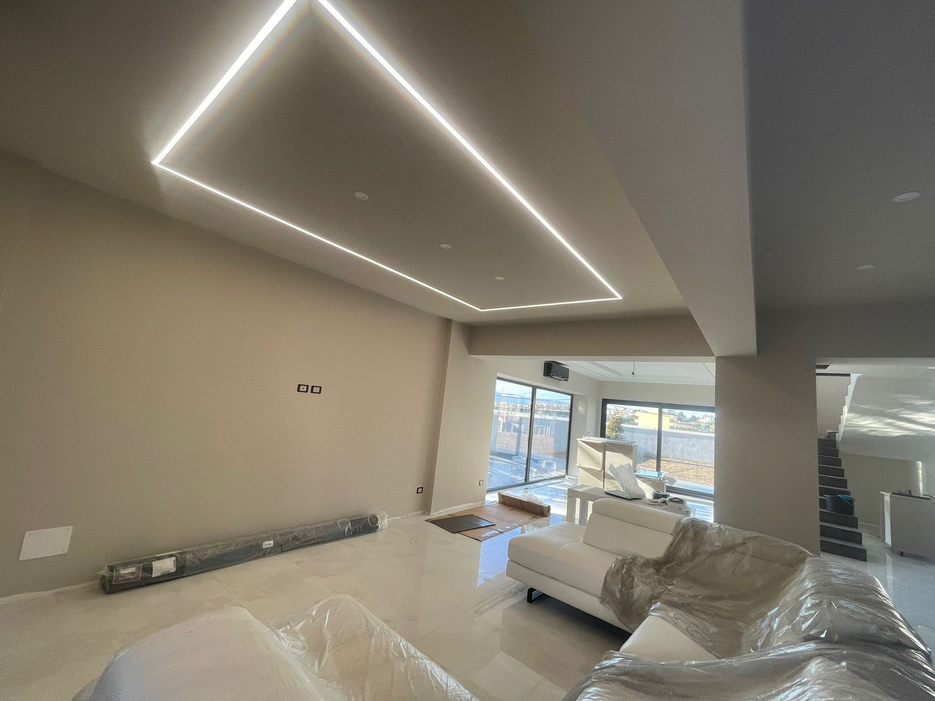 Interni moderni con illuminazione quadrata da incasso nel soffitto, pareti beige e pavimento piastrellato bianco.