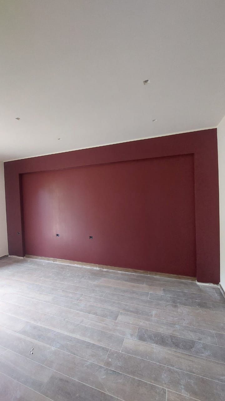 Stanza vuota con una parete caratteristica color marrone e soffitto bianco. Pavimento in legno grigio.