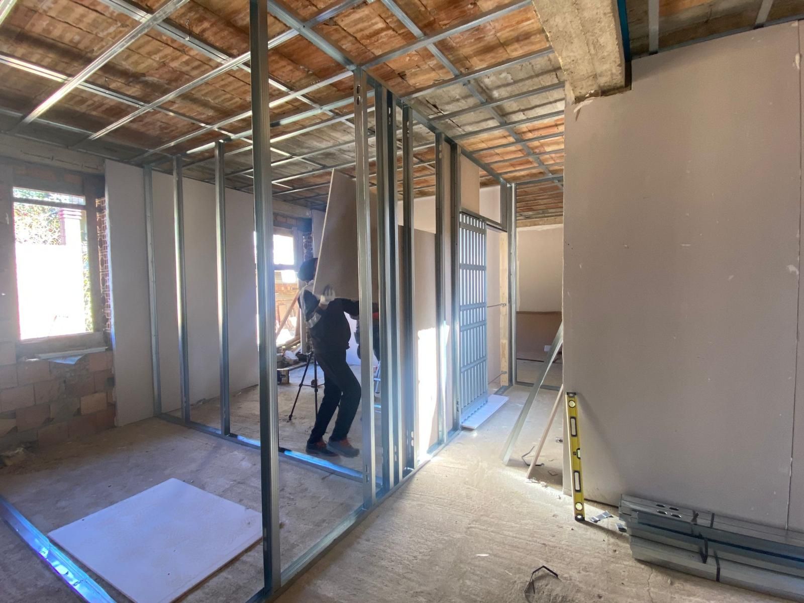 Stanza interna in costruzione: persona al lavoro su una parete in metallo, cartongesso parzialmente installato.