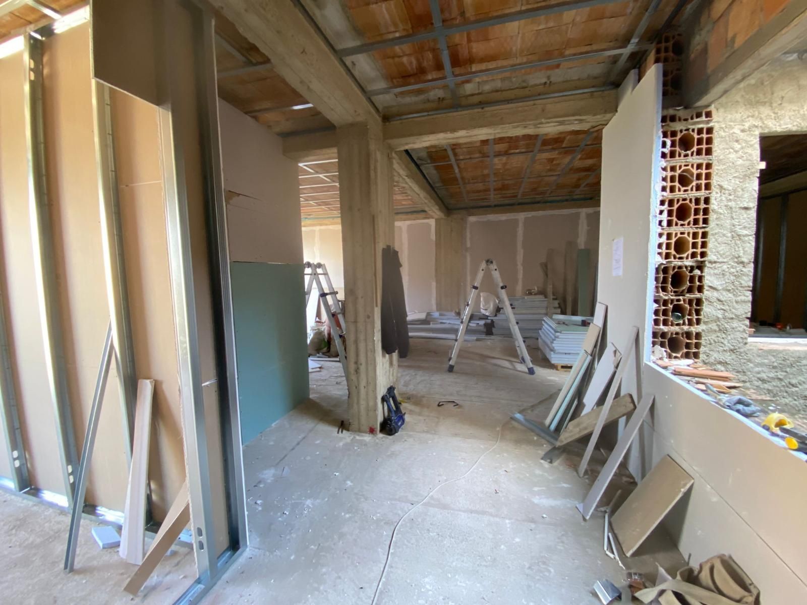 Ristrutturazione interna di una stanza con installazione di cartongesso in corso; pavimento in cemento e mattoni a vista.