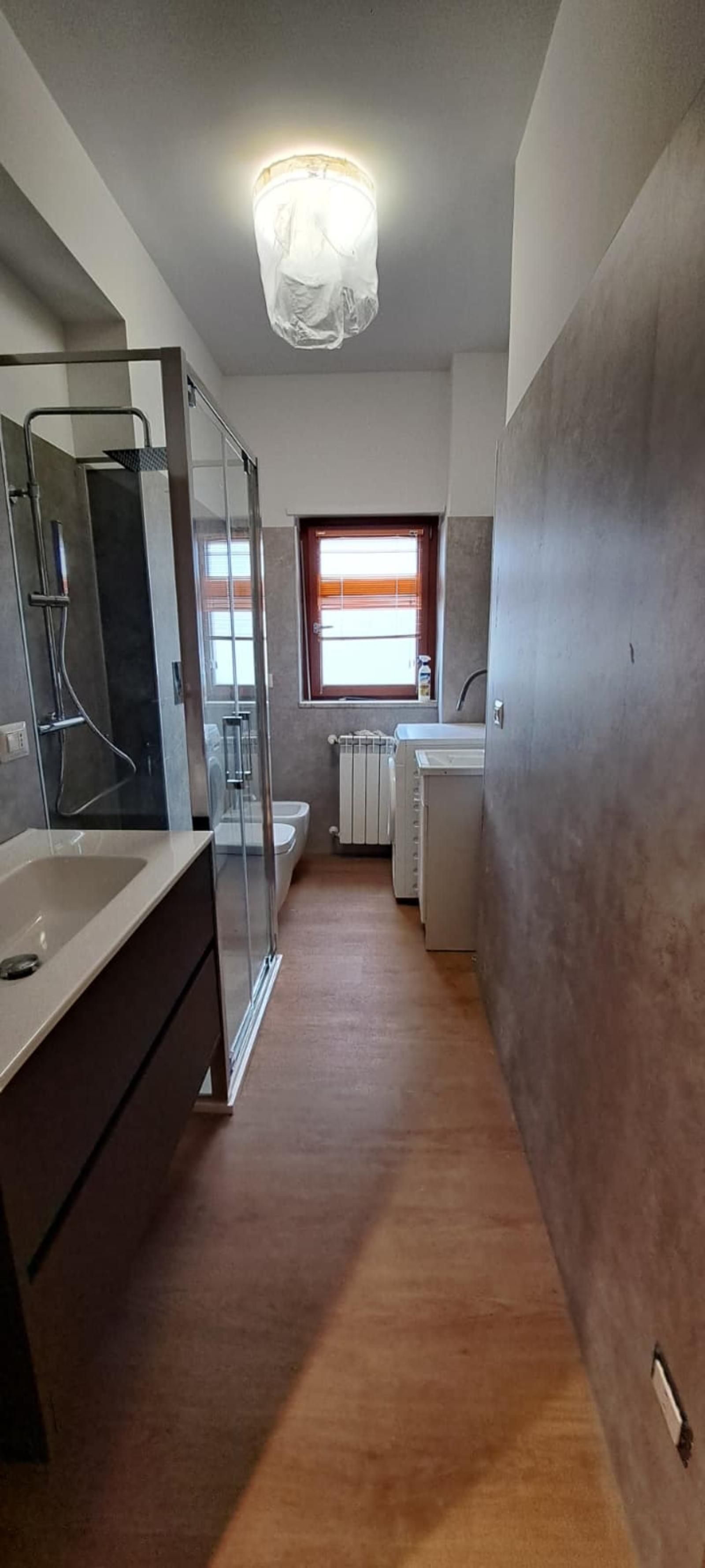 Un bagno stretto con doccia, WC e lavandino. Pavimento e pareti marroni e una finestra.